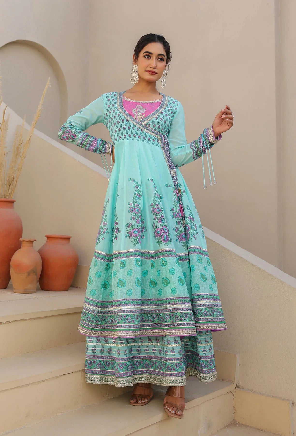 Woman in a traditional outfit standing on steps with decorative vases in the background