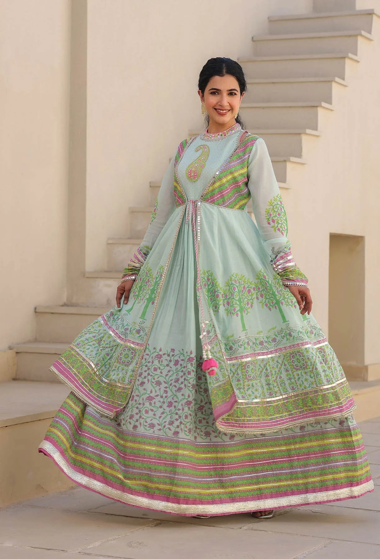 Woman in a traditional light green and pink embroidered outfit standing on steps.