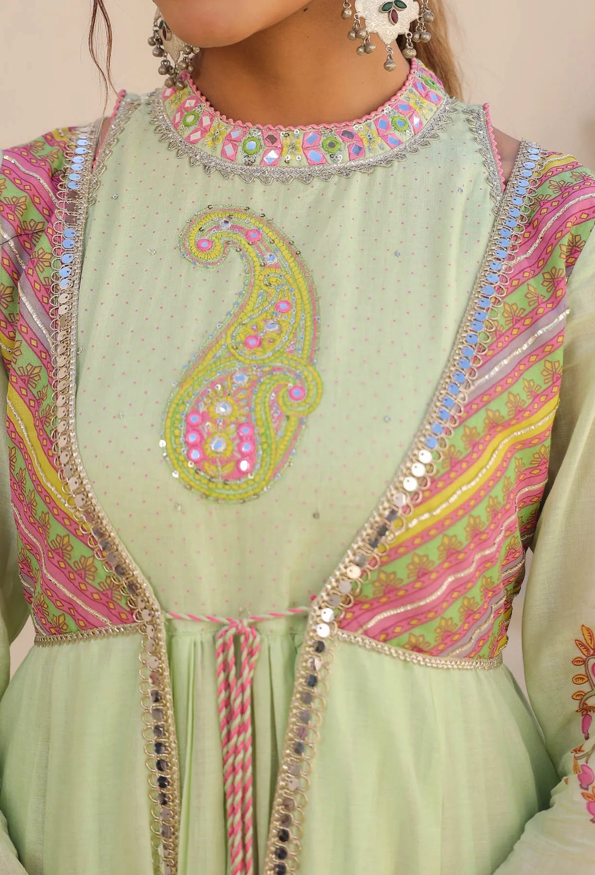Light green traditional outfit with intricate pink and yellow embroidery on a beige background