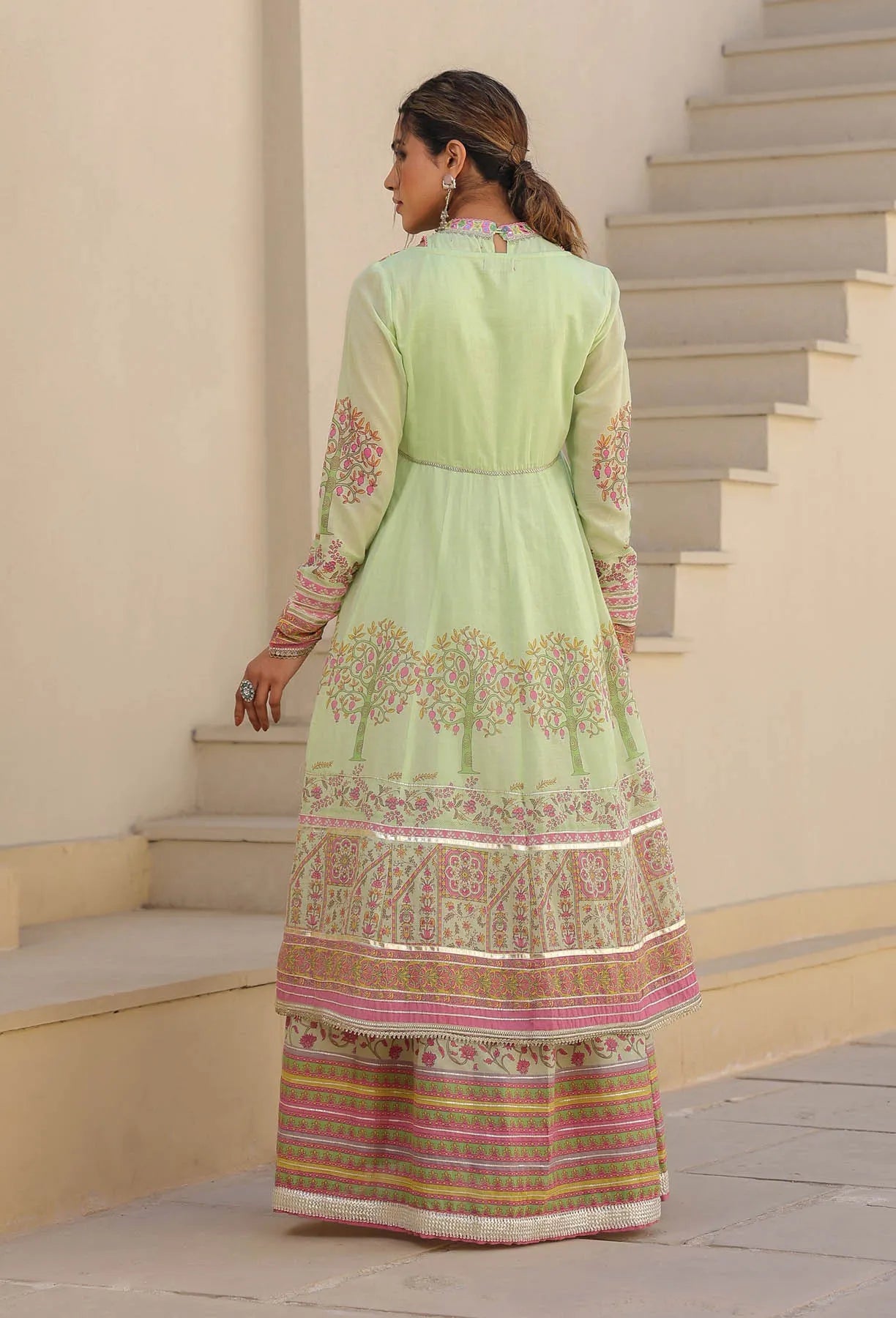 Woman in a light green traditional outfit with floral patterns standing on a staircase.