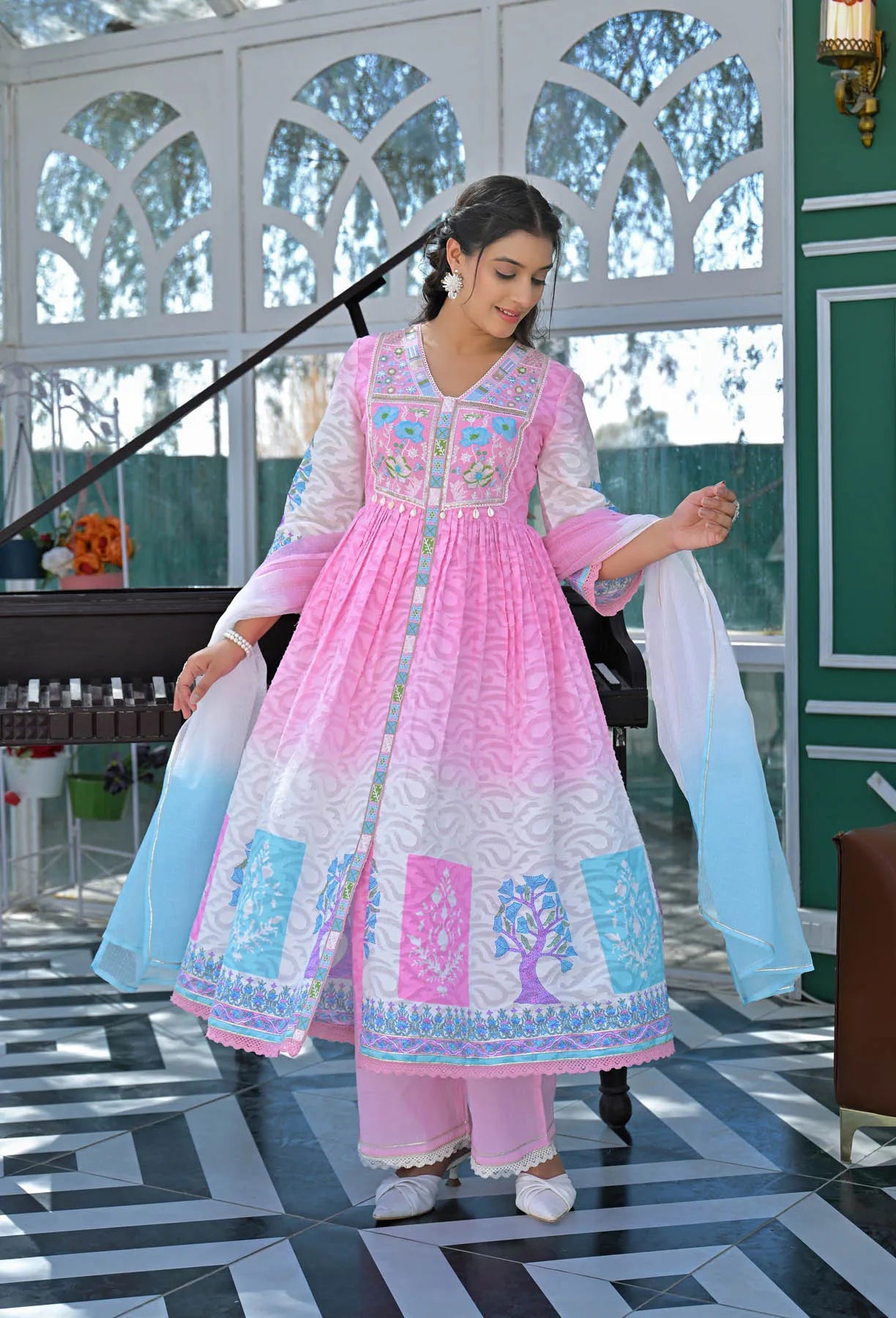 Woman in a pink and white traditional outfit with floral patterns in a decorated room.
