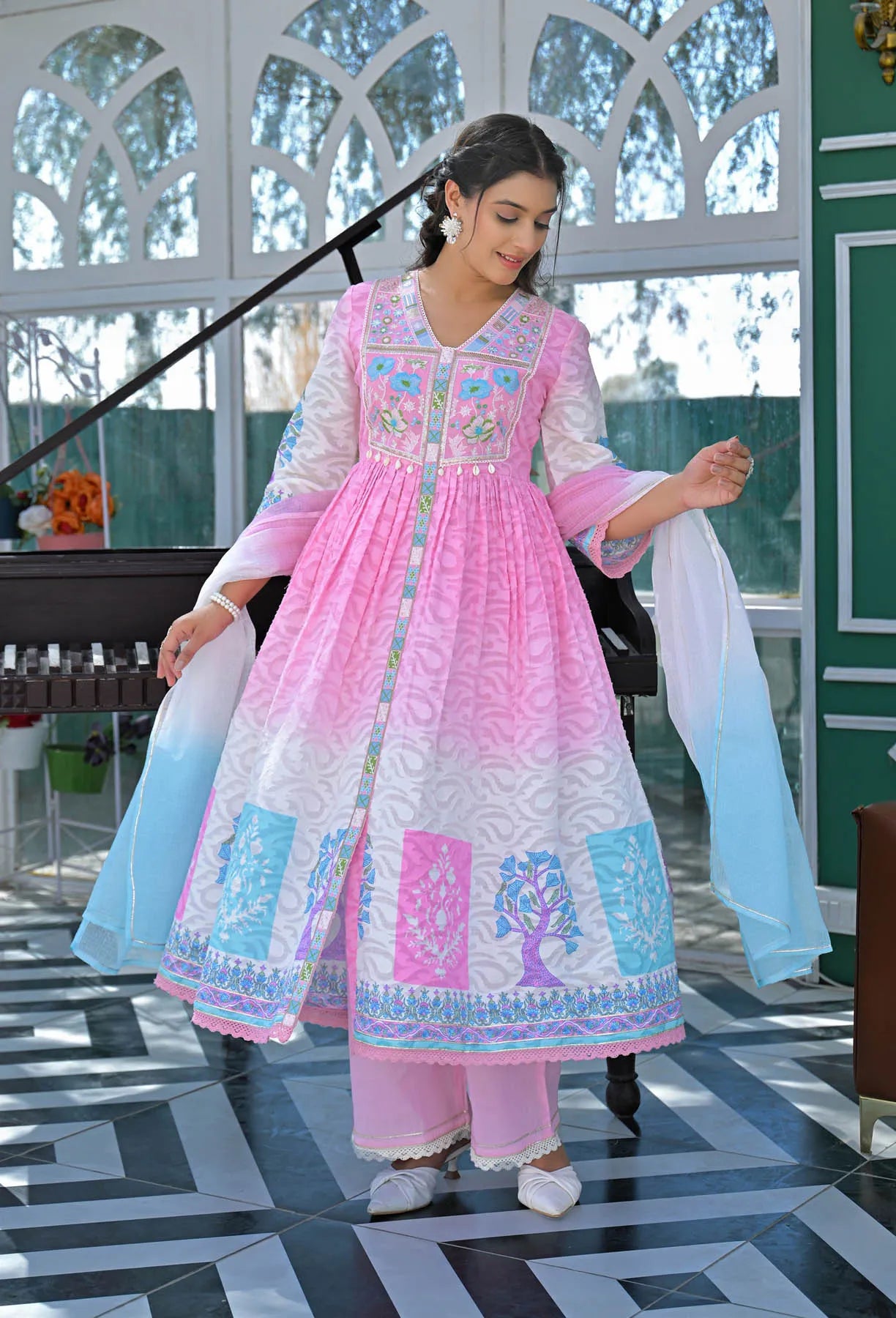Woman in a pink and white traditional outfit with blue patterns in an indoor setting.