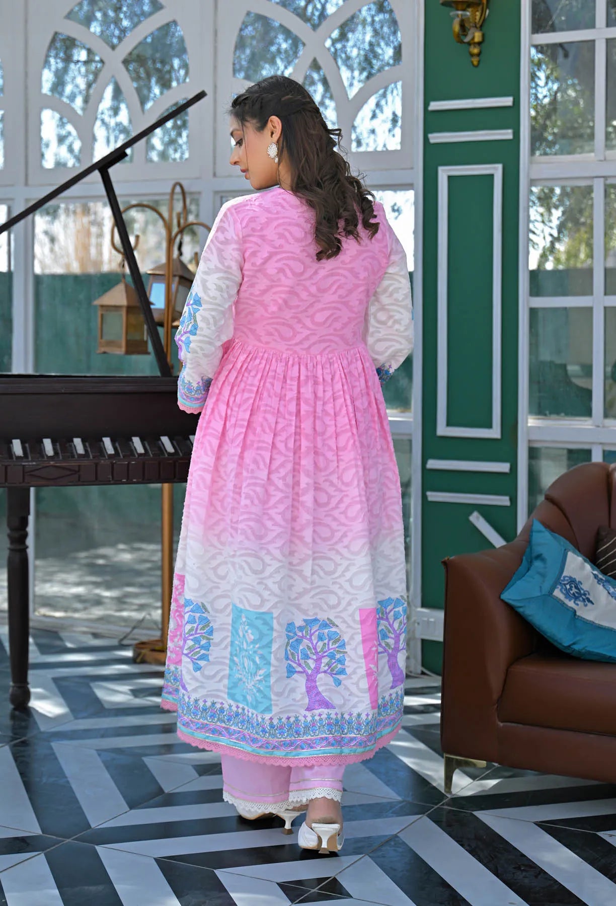 Woman in a pink traditional outfit walking in a decorated room with a piano and sofa.