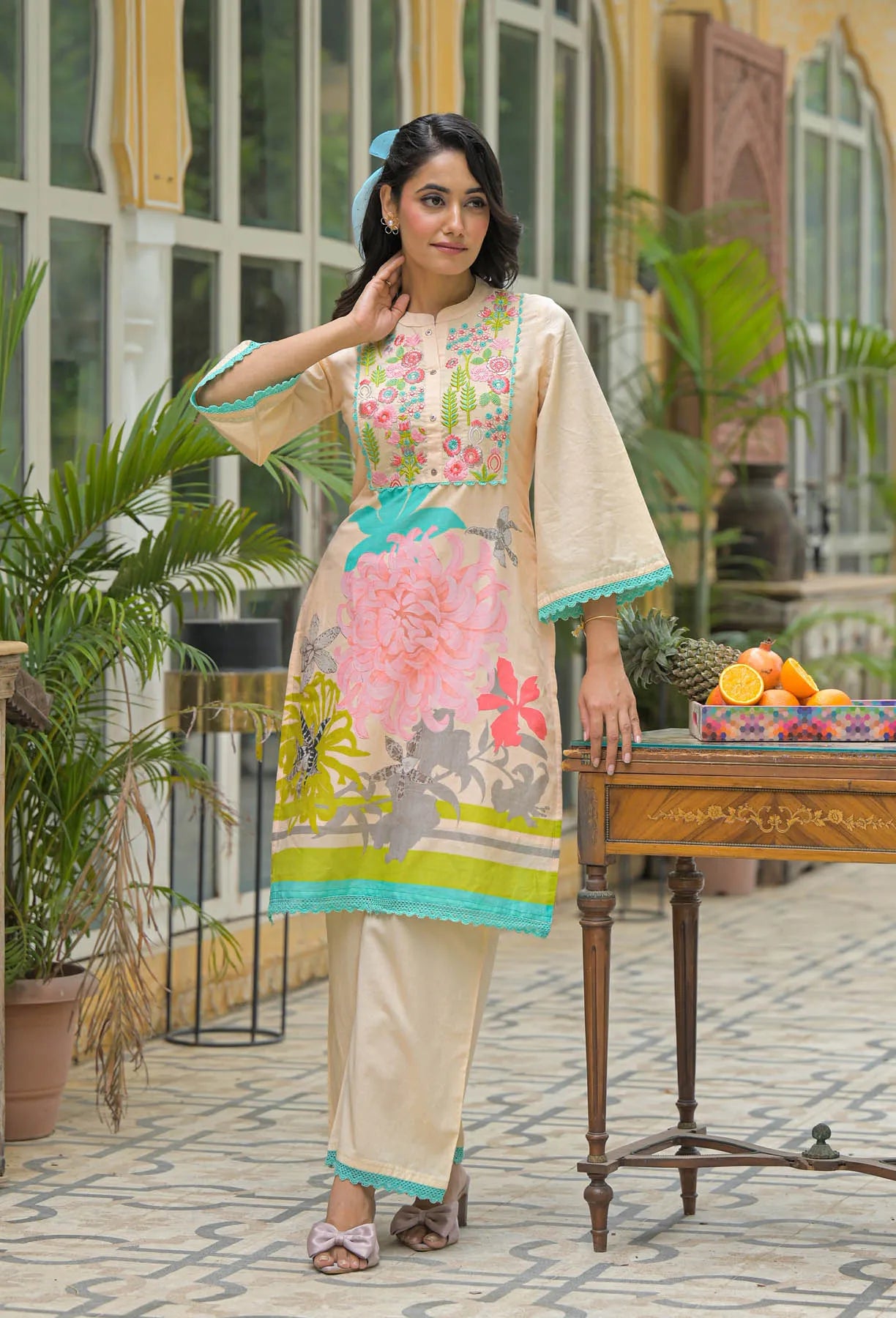 Woman in a floral dress standing in an outdoor setting with plants and a table.