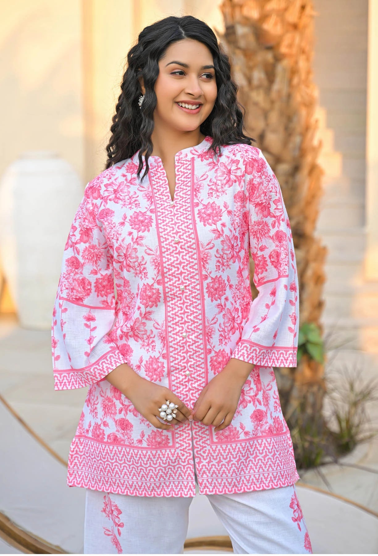 Woman wearing a pink and white patterned outfit with a blurred outdoor background