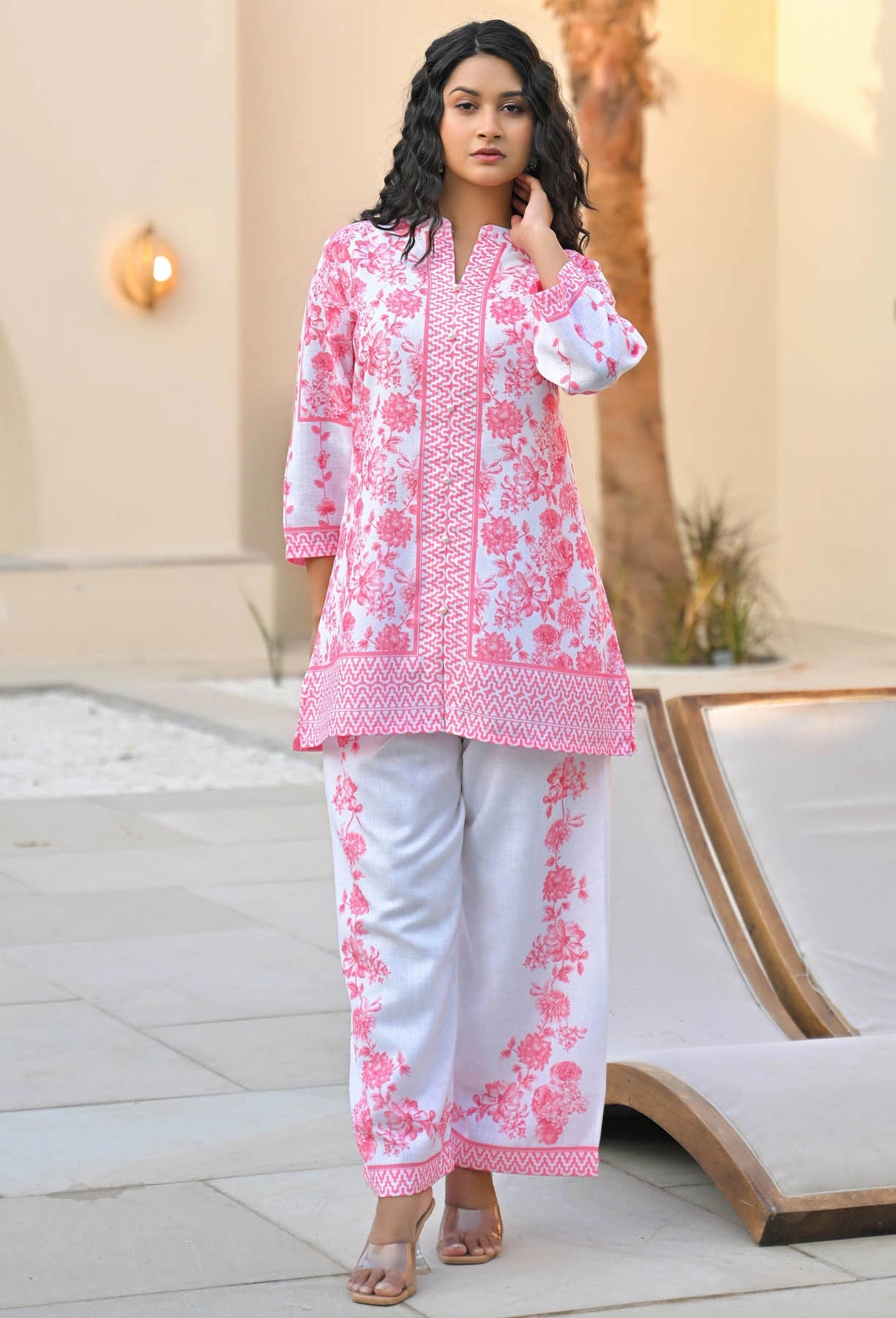 Woman wearing a pink and white floral outfit standing outdoors.