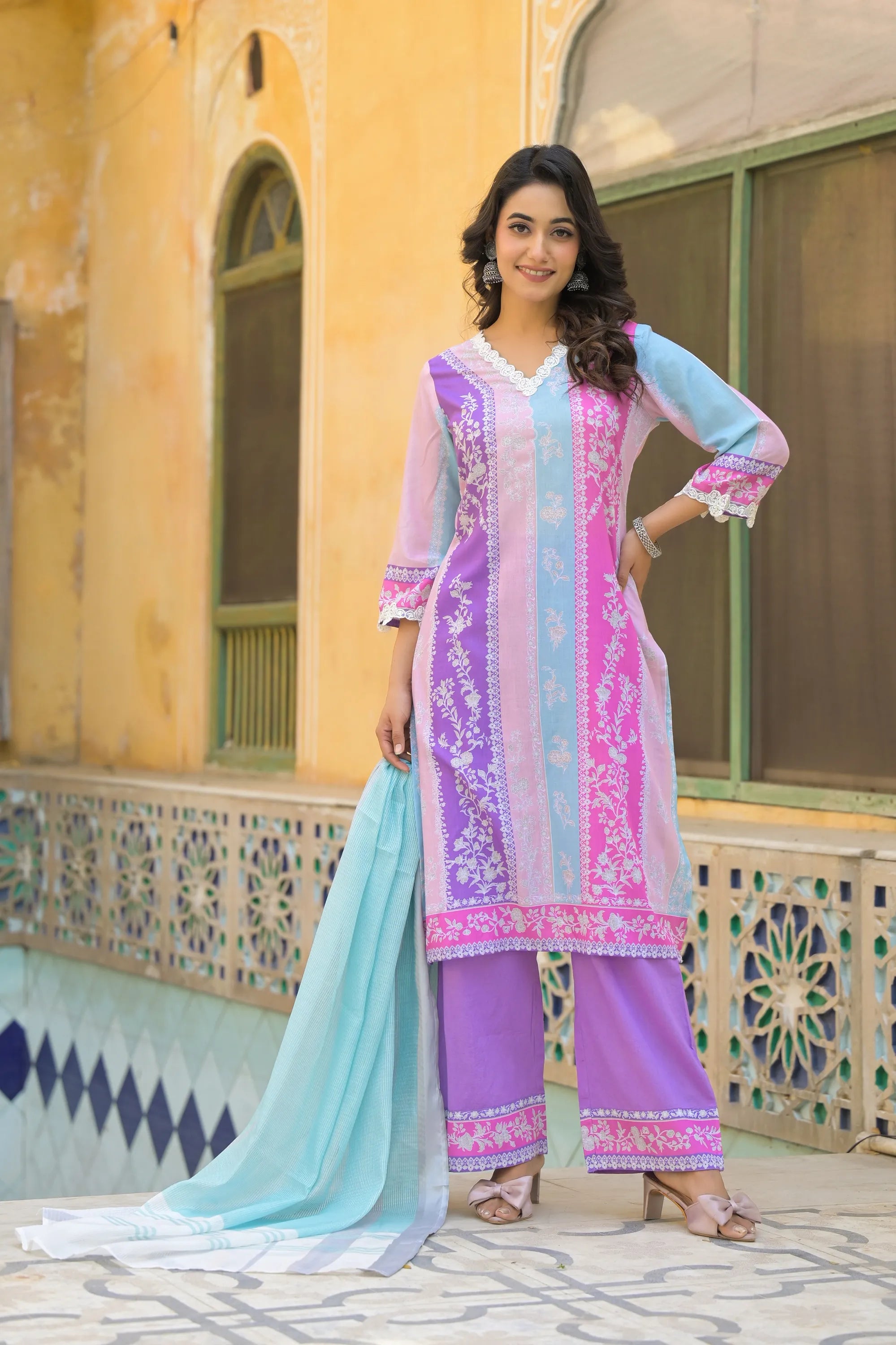 Woman in a colorful traditional outfit standing in front of a decorative building.
