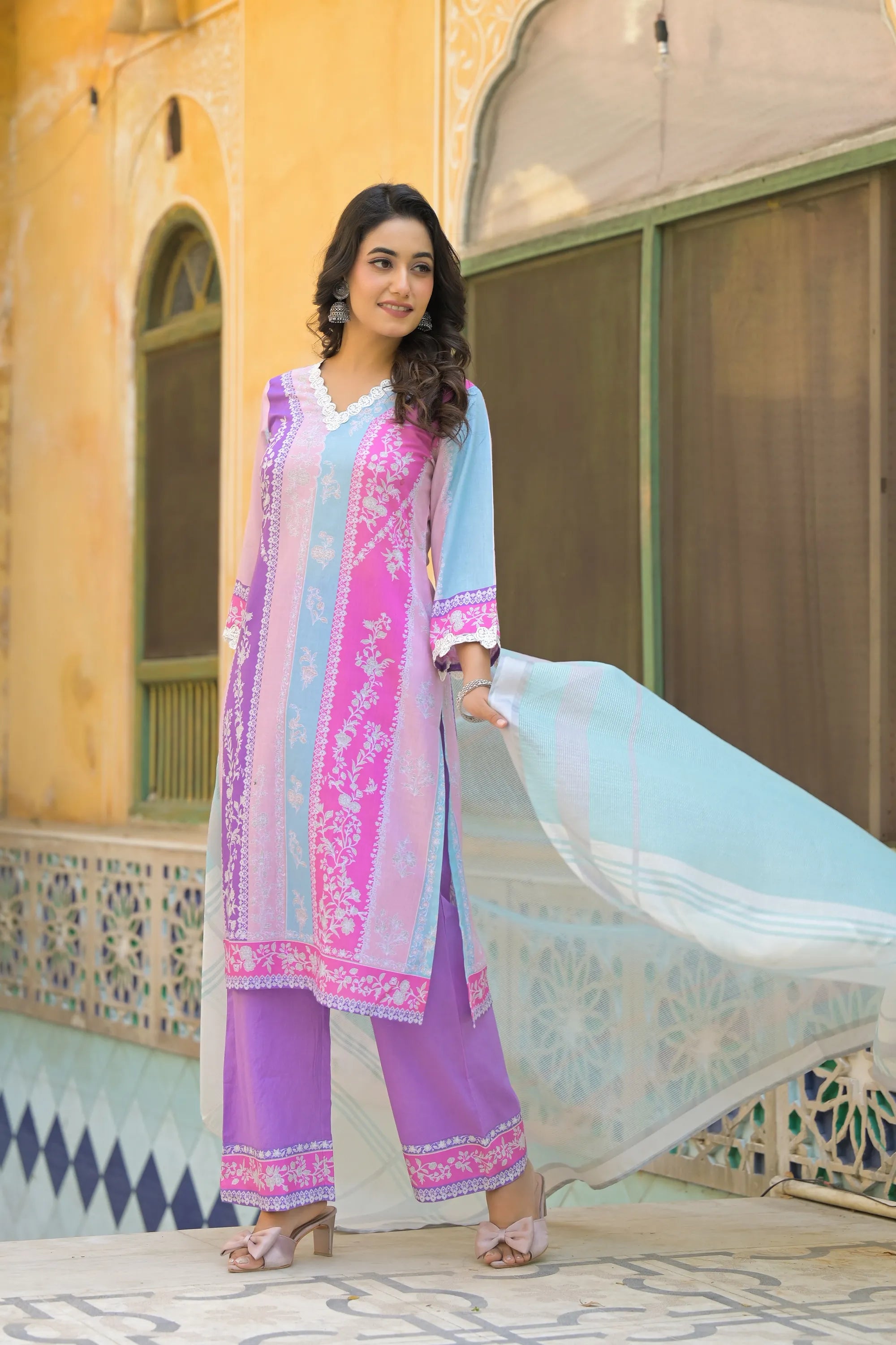 Woman in a traditional outfit with a colorful dupatta standing in front of an architectural background.