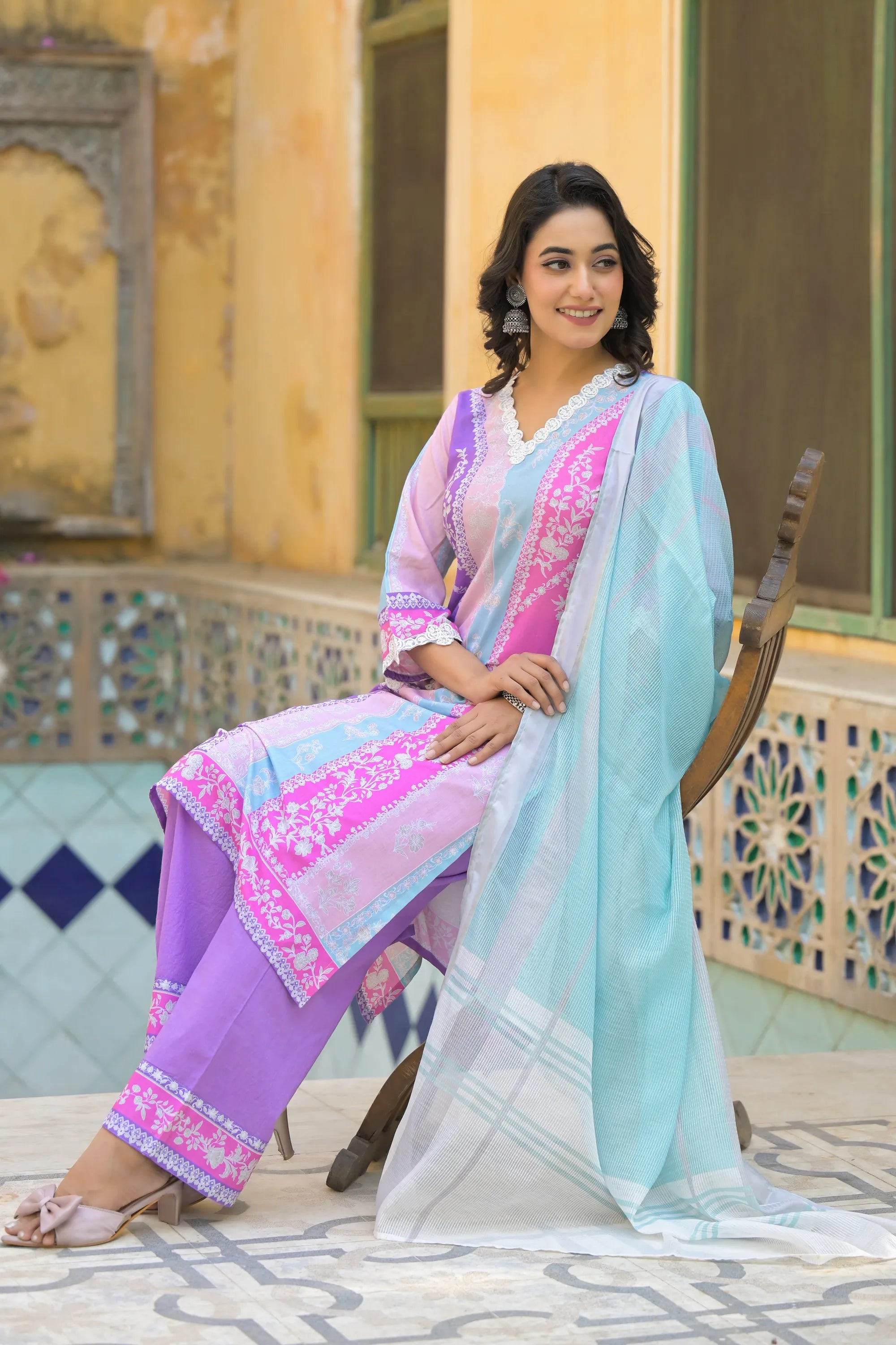 Woman in a colorful traditional outfit sitting outdoors with decorative columns in the background