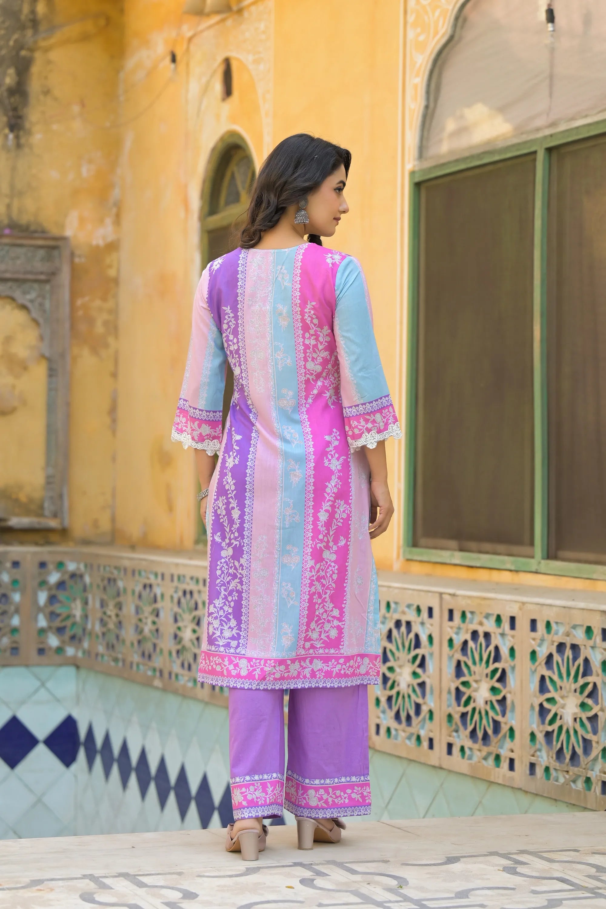Woman in a colorful traditional outfit standing in front of a decorative wall.