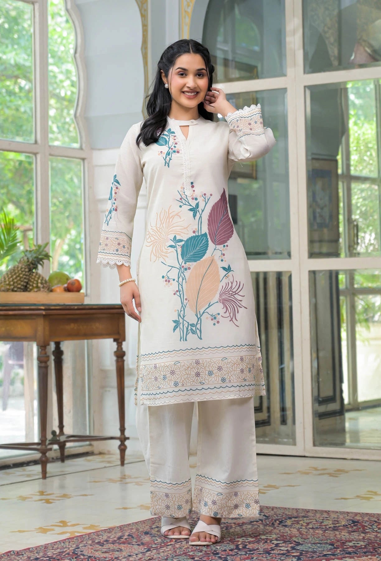 Woman wearing a white embroidered outfit in a bright room with large windows.