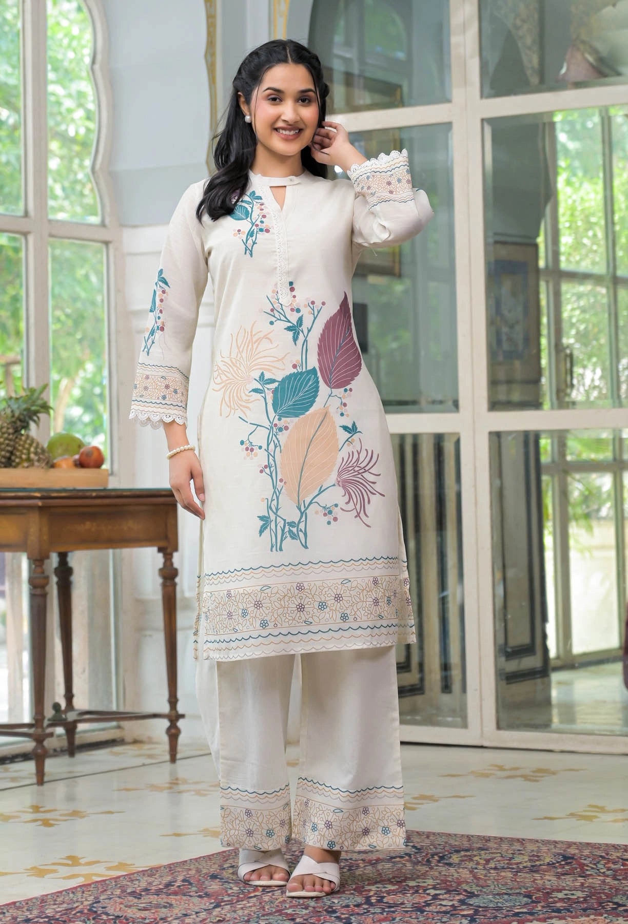 Woman wearing a white embroidered outfit in a room with large windows.