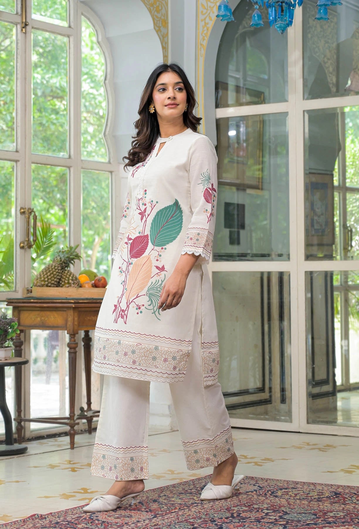 Woman wearing a white embroidered outfit in a bright room with large windows.