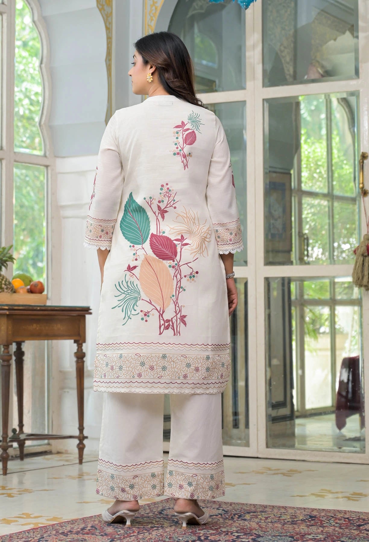 Woman wearing a white embroidered outfit in a decorated room.