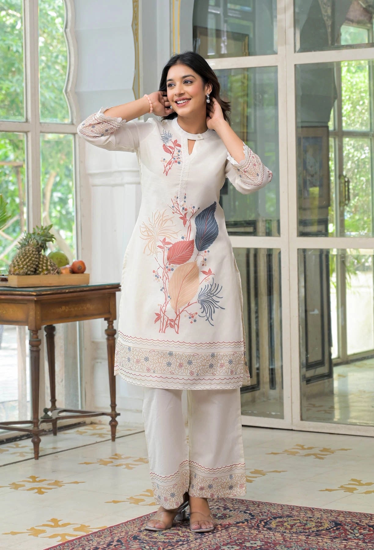 Woman wearing a white embroidered outfit in a bright room with large windows.