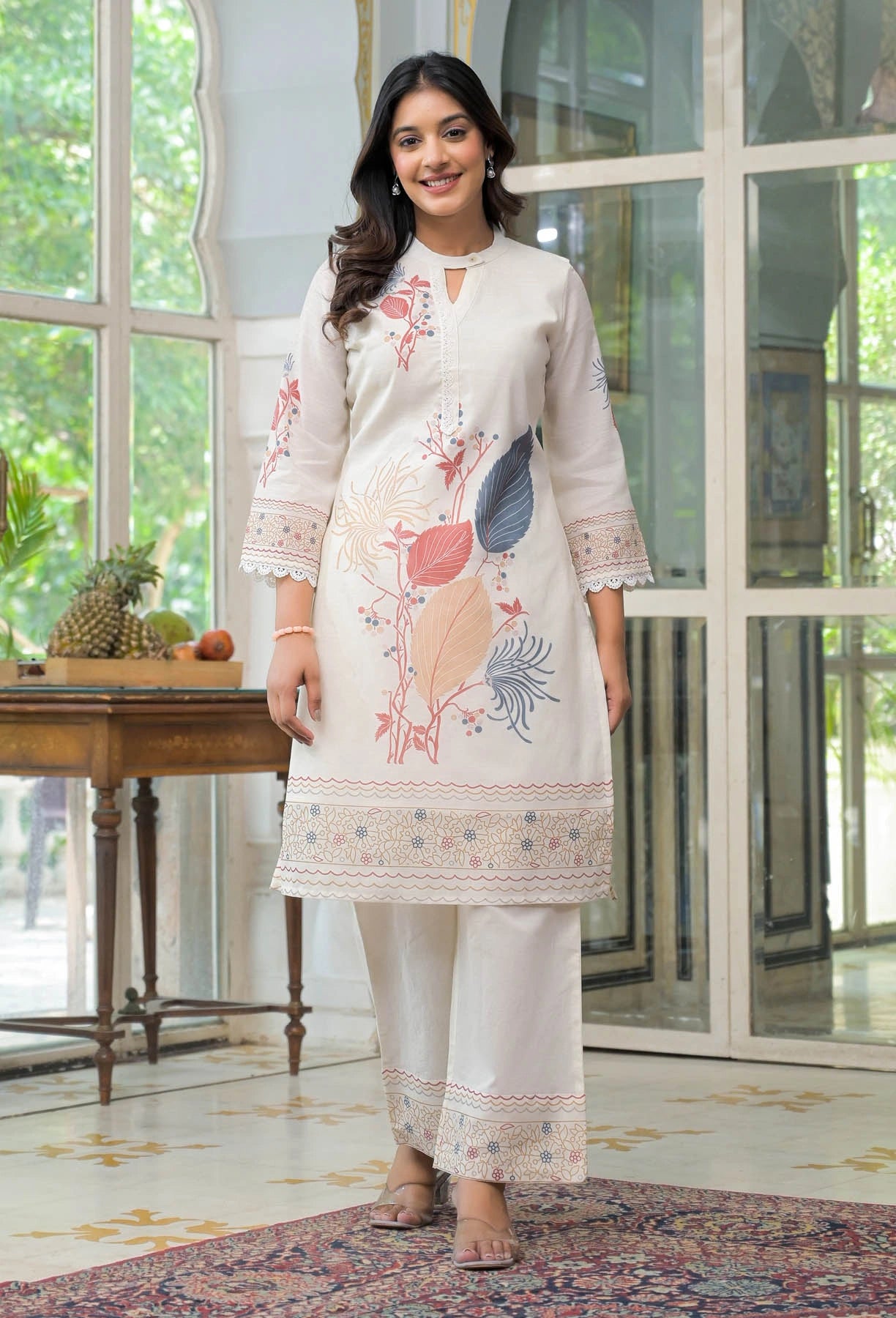 Woman wearing a white embroidered outfit in a room with large windows.