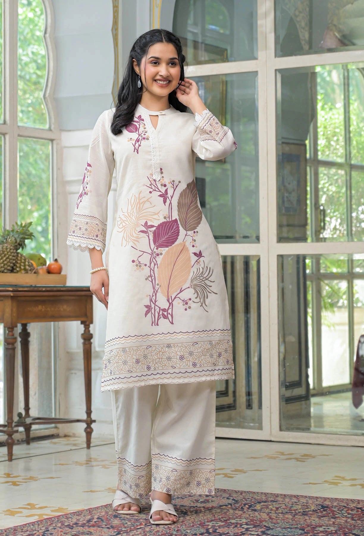 Woman wearing a white embroidered outfit standing in a room with large windows.