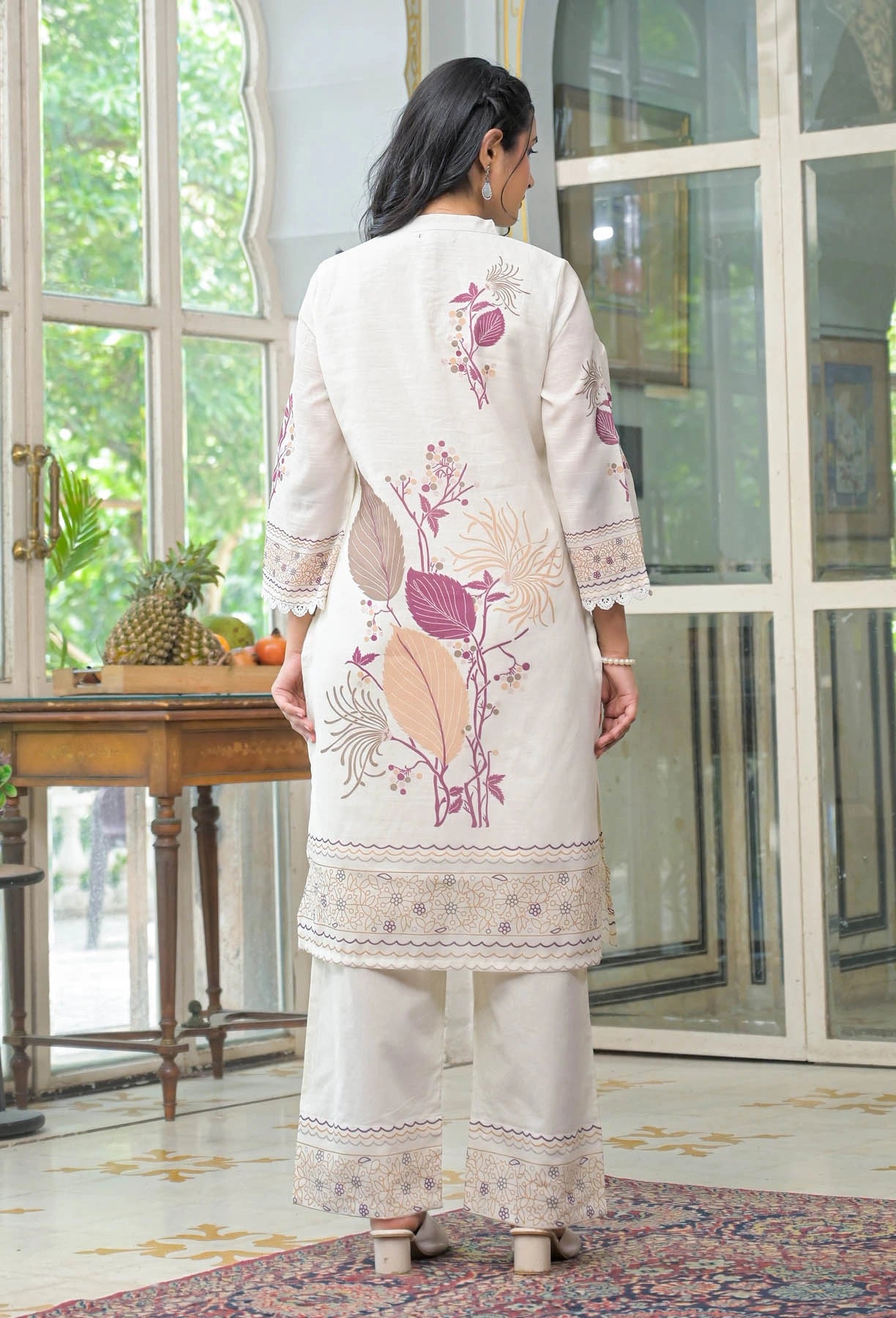 Woman wearing a white embroidered outfit in a room with large windows.