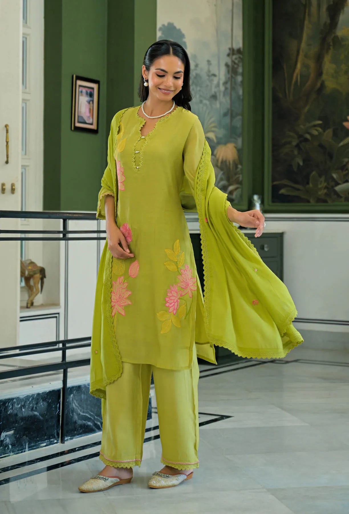 Woman in a green traditional outfit with floral embroidery in an indoor setting.