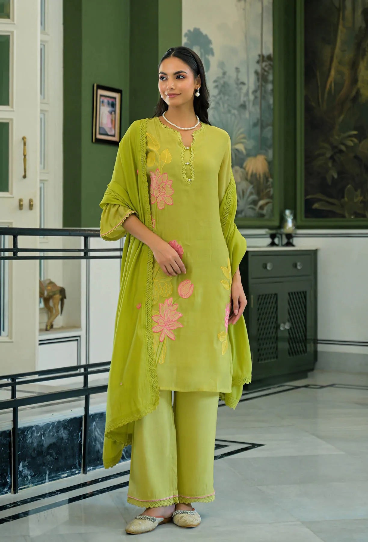Woman wearing a green traditional outfit with floral patterns in an indoor setting.