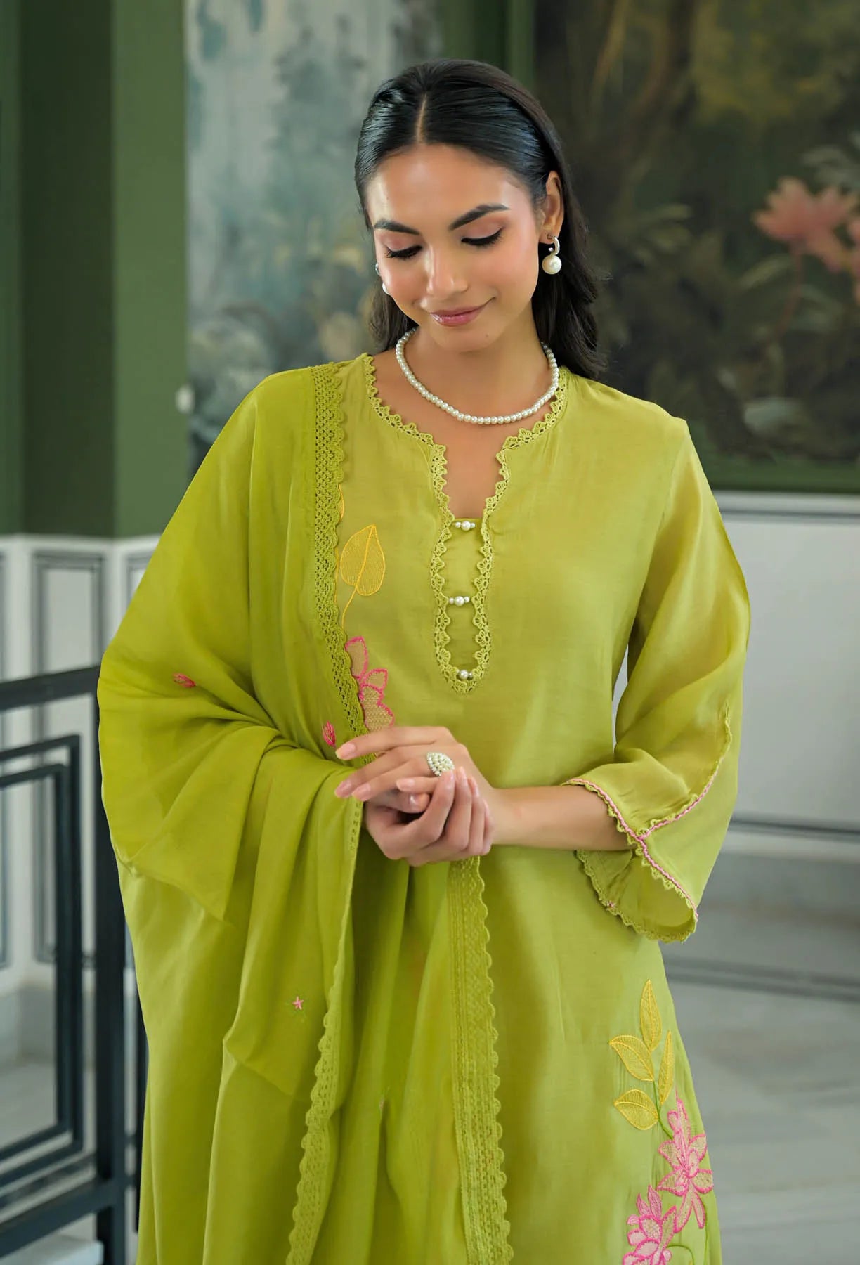 Woman wearing a green traditional outfit with floral patterns indoors.