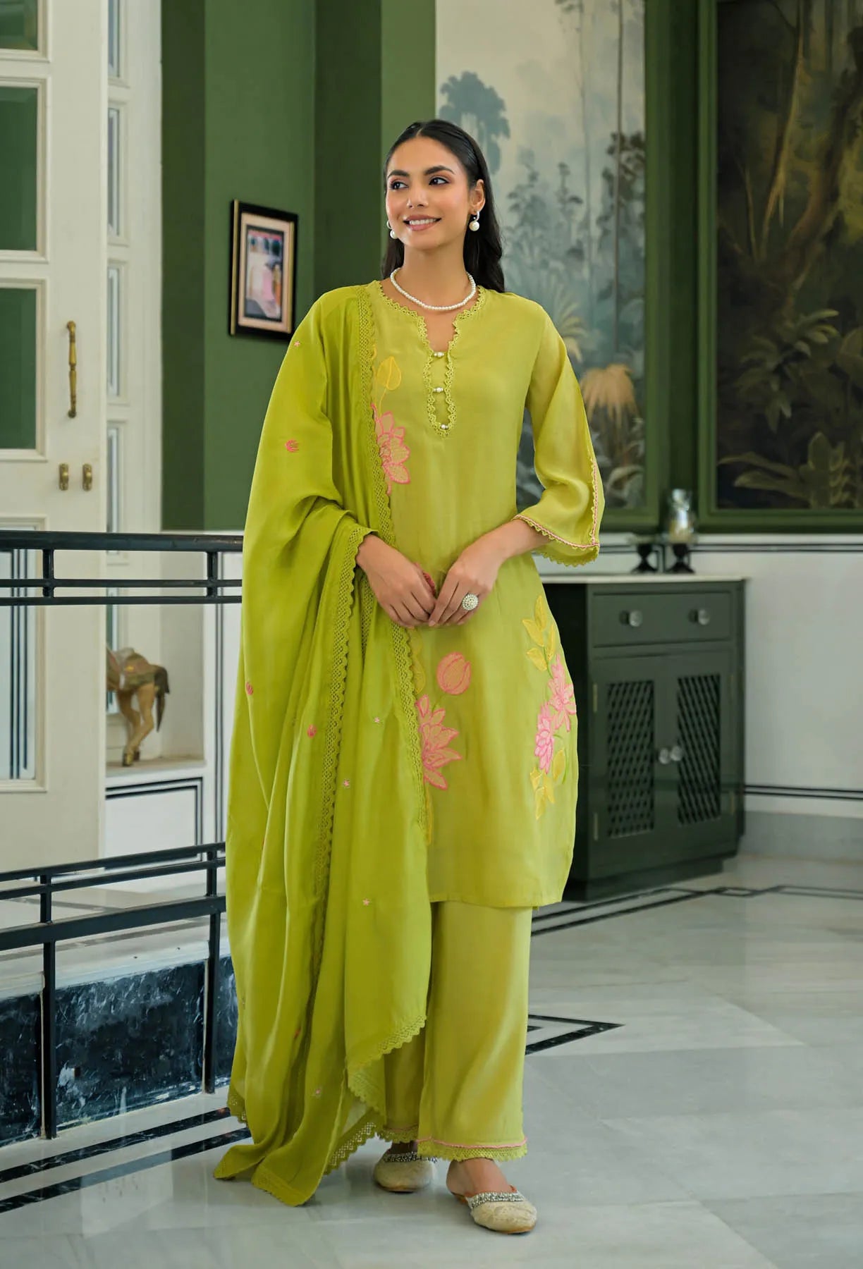 Woman in a green traditional outfit standing in a room with decorative elements.