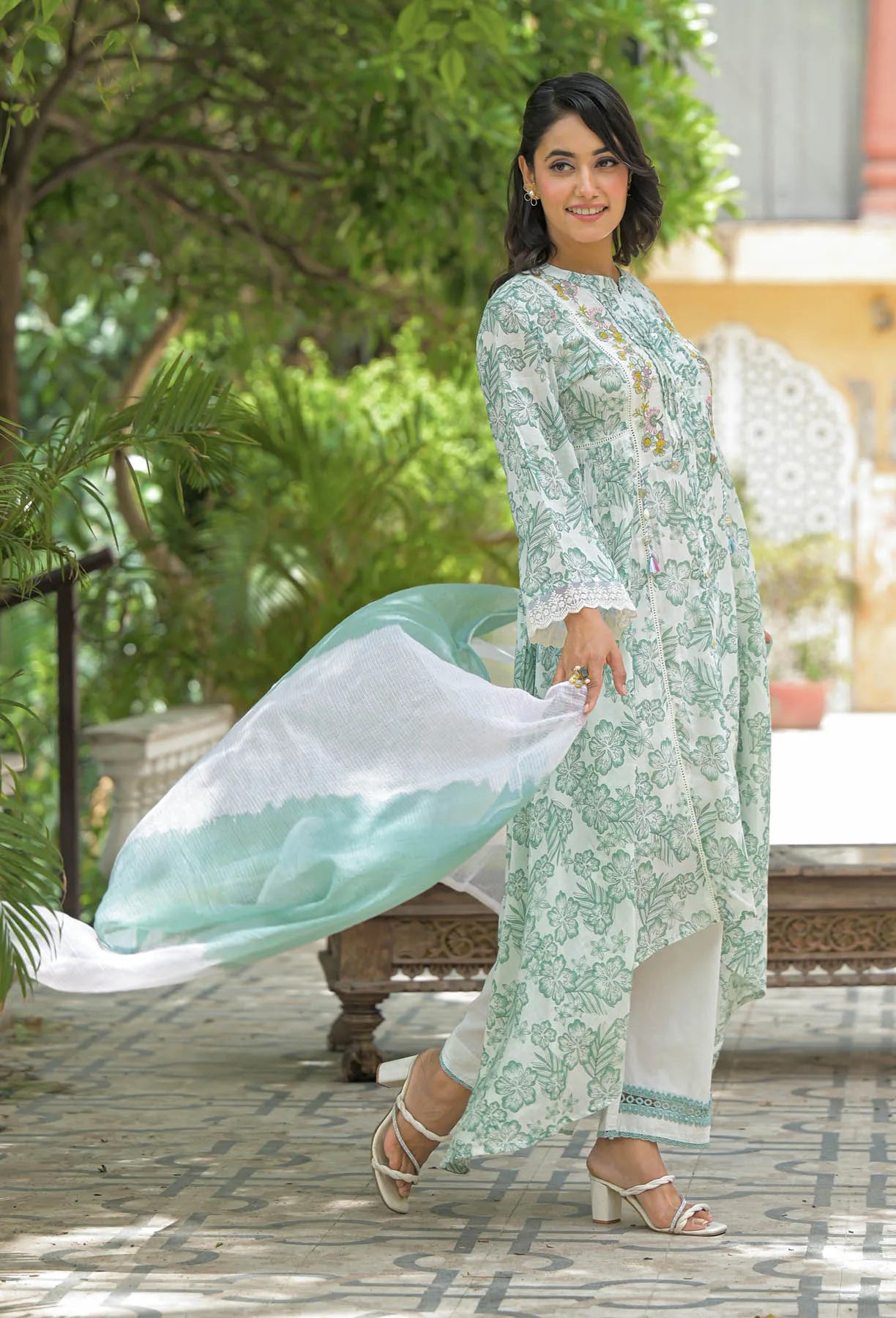 Woman in a light green and white traditional outfit standing outdoors with greenery in the background