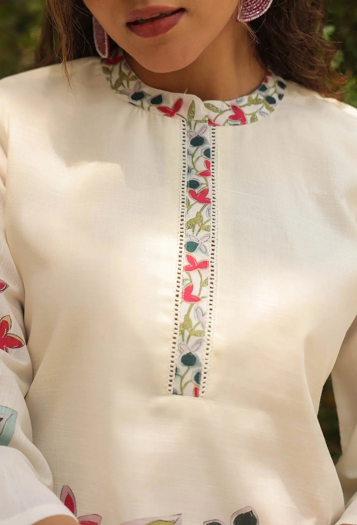 Close-up of a cream-colored top with floral embroidery on a blurred natural background