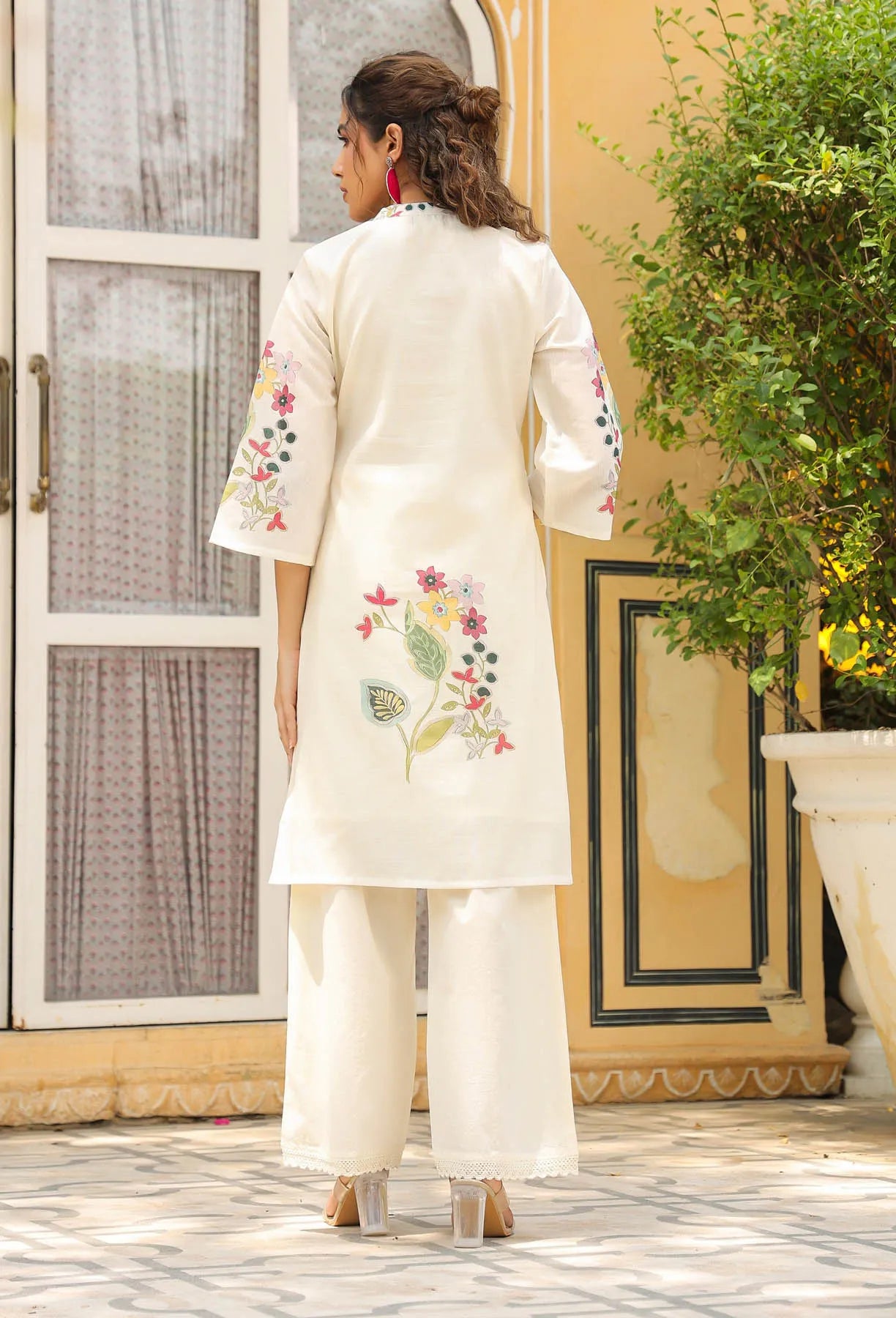 Woman wearing a white embroidered outfit standing in a decorative indoor setting.