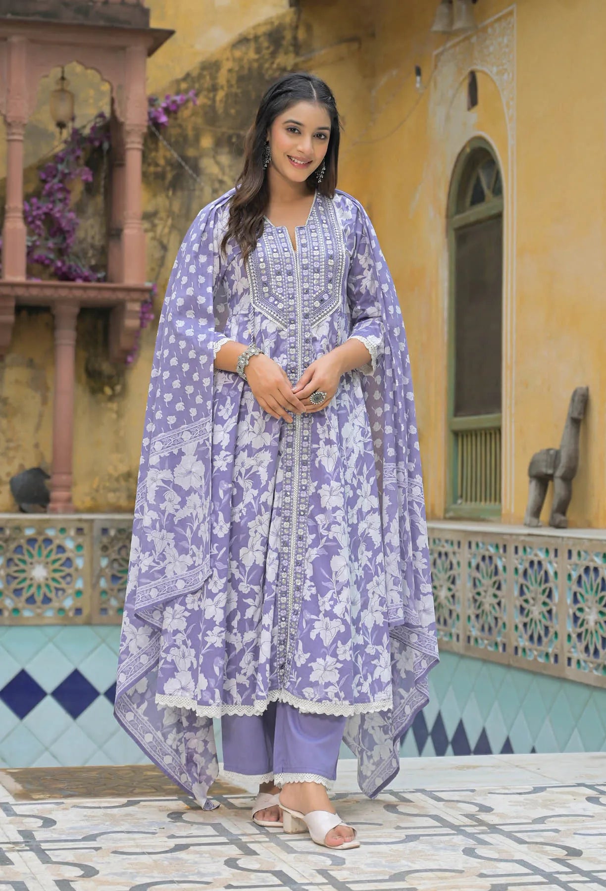 Woman in a purple floral outfit standing in front of a colorful architectural background