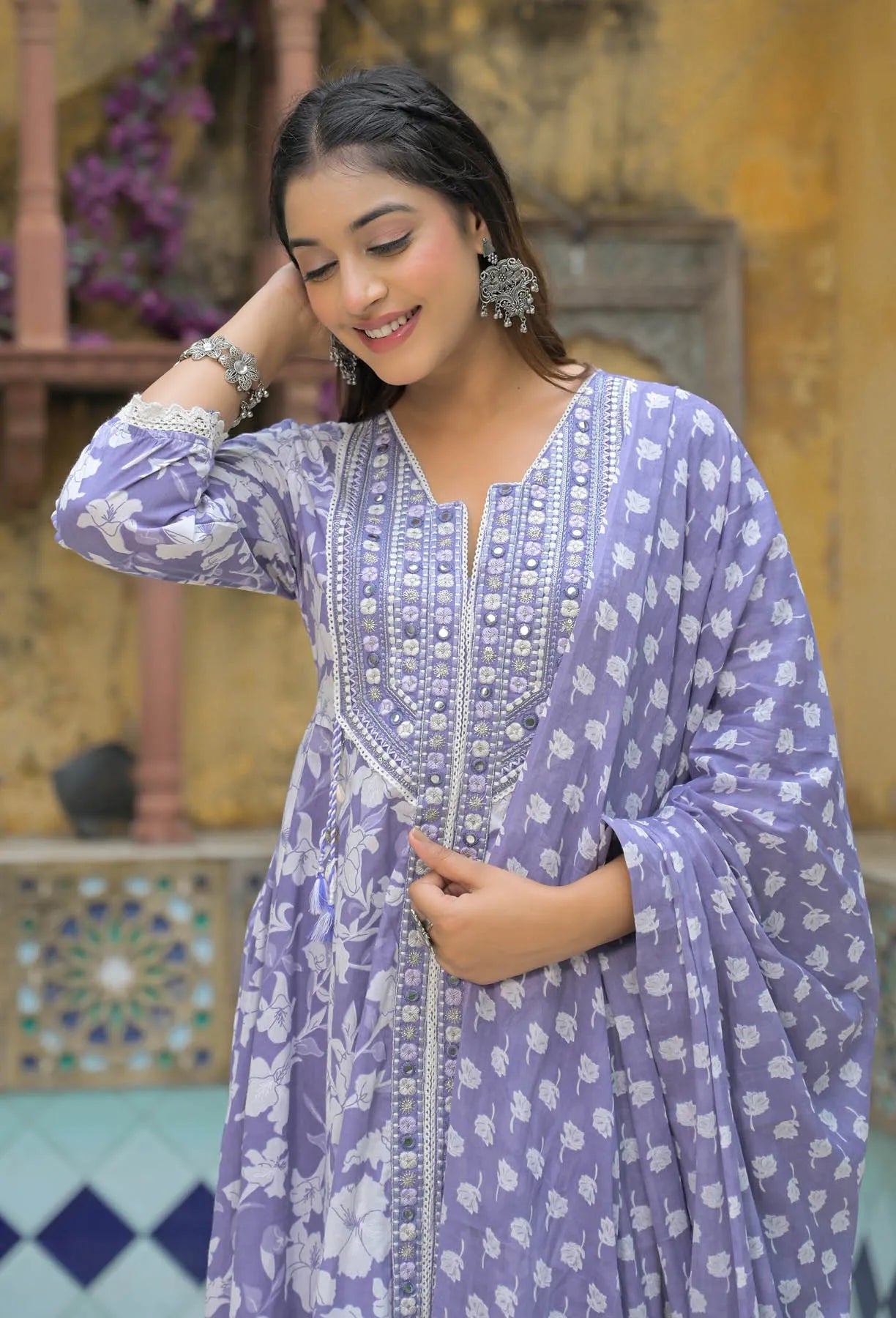 Woman wearing a purple traditional outfit with floral patterns in an outdoor setting.