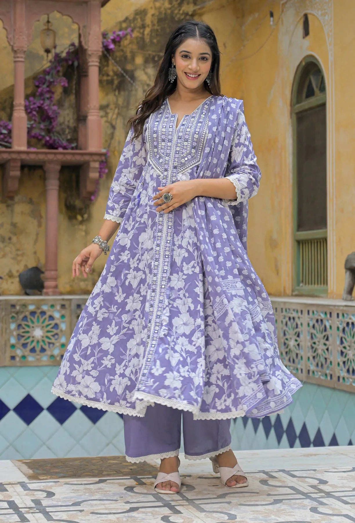 Woman in a purple floral outfit standing in front of a decorative wall.