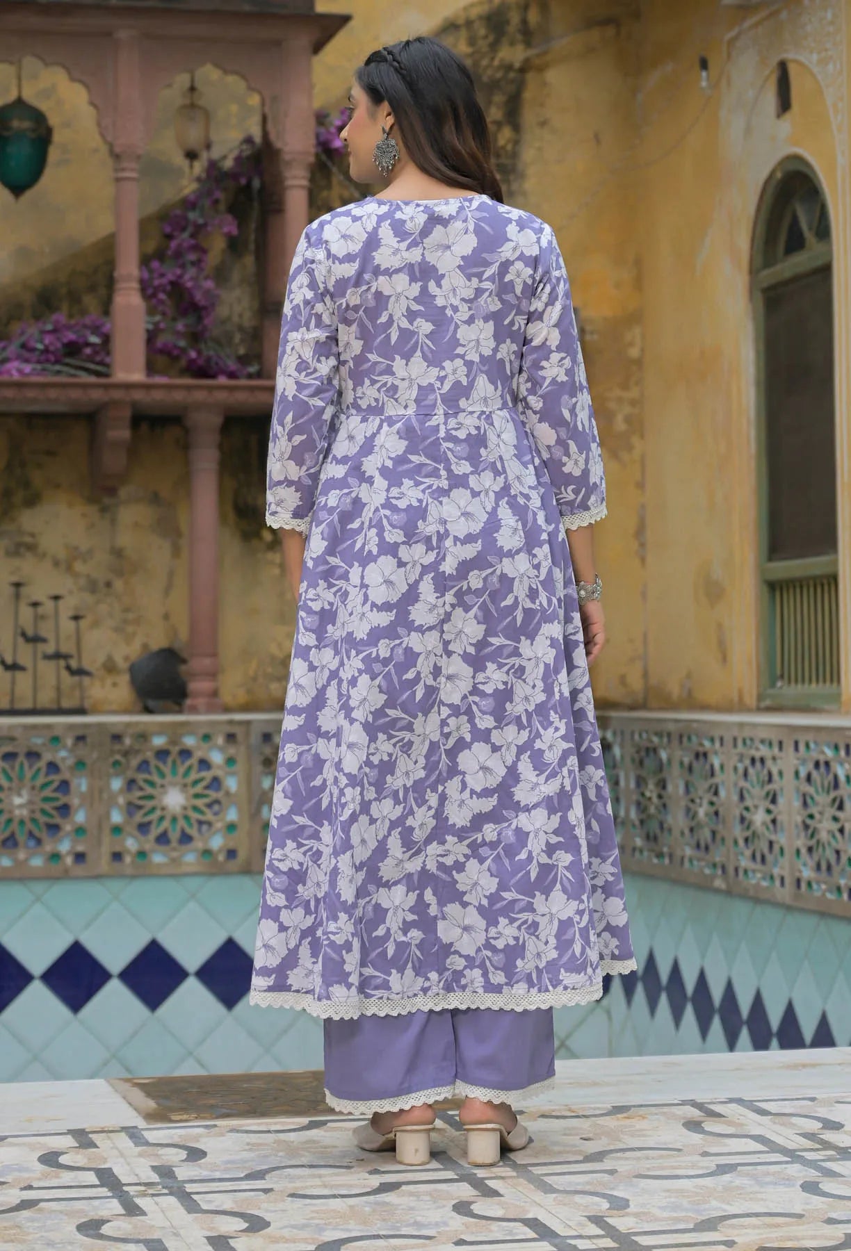 Woman wearing a purple floral outfit standing in front of a decorative building.