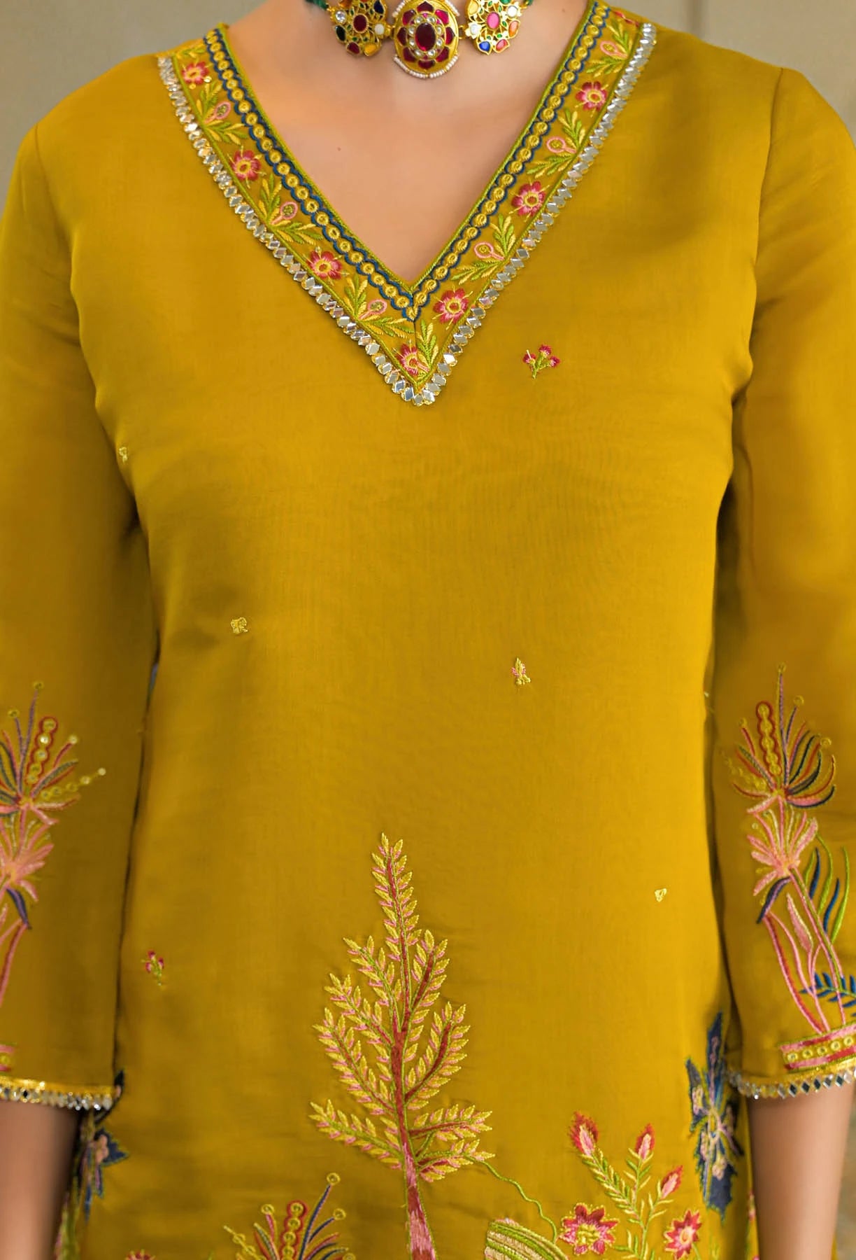 Mustard yellow traditional outfit with intricate embroidery and a necklace.