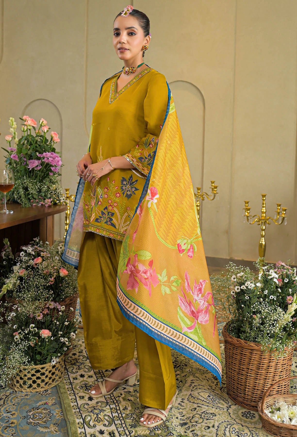 Woman in a traditional outfit with a floral shawl in a decorated room.