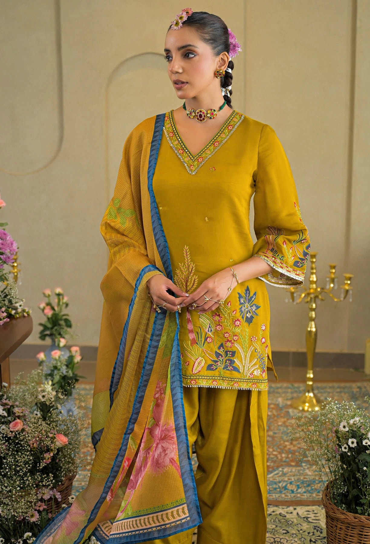 Woman in a yellow traditional outfit with floral patterns in an indoor setting.