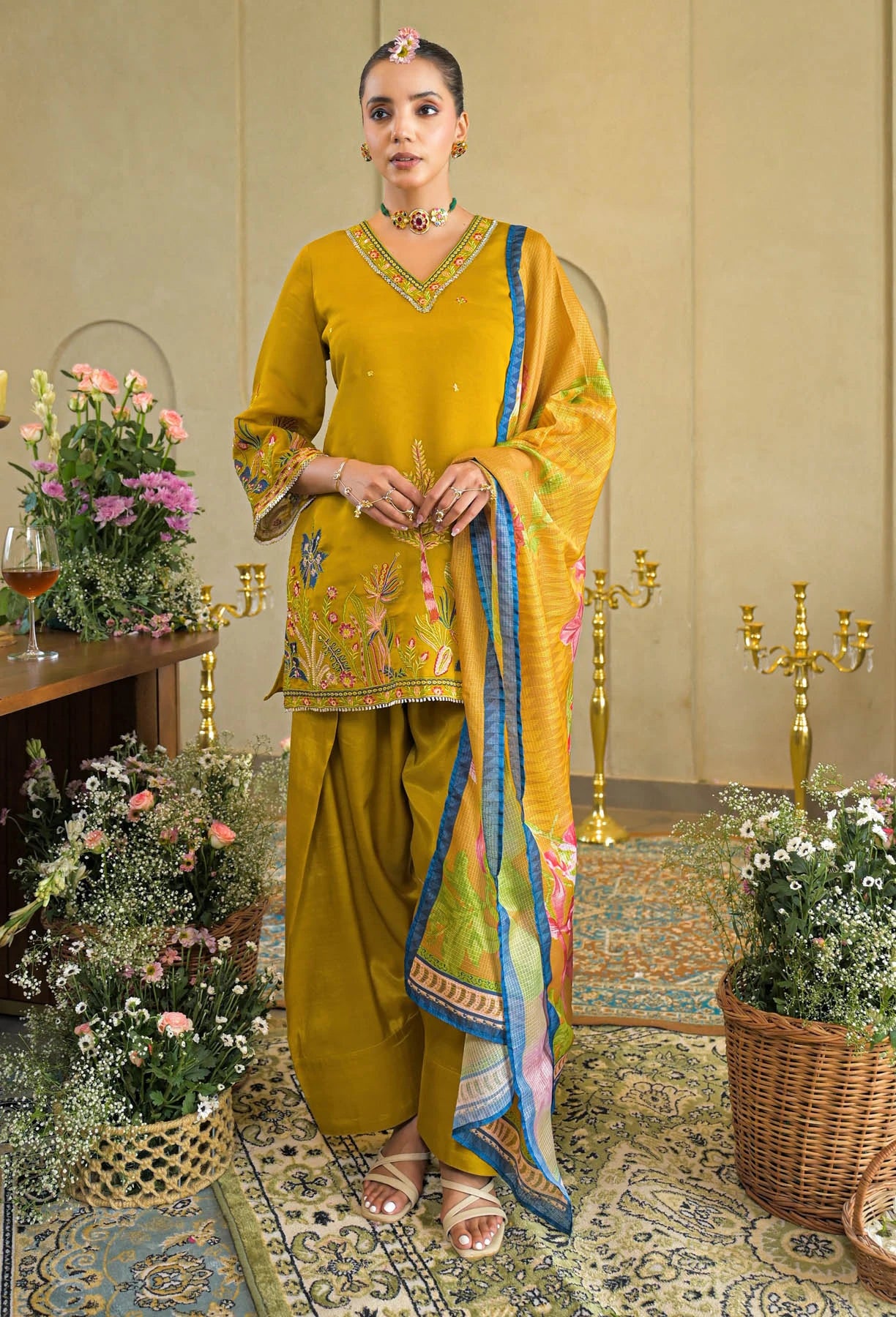 Woman in a yellow traditional outfit standing in an elegant room with floral decorations.