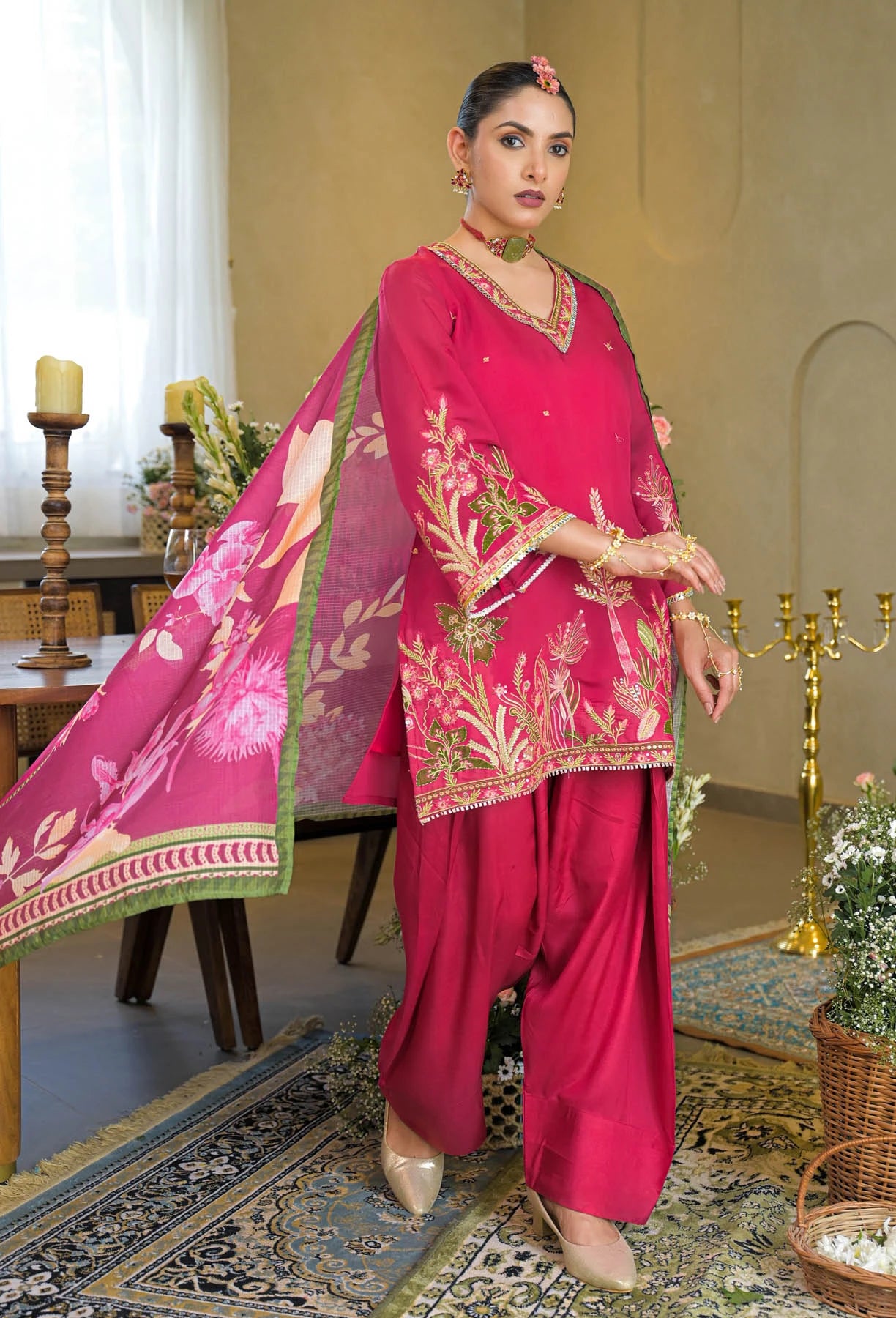 Woman in a traditional pink outfit with floral patterns in an elegant indoor setting.