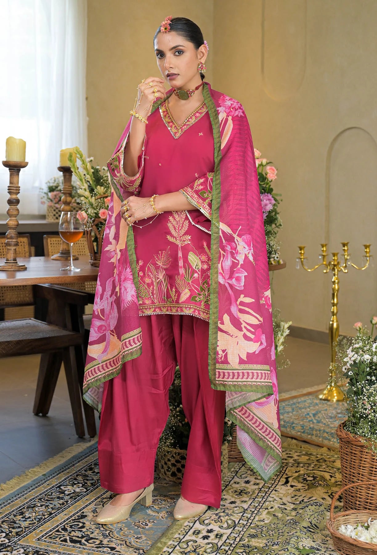 Woman in a pink traditional outfit with floral patterns in an elegant room.