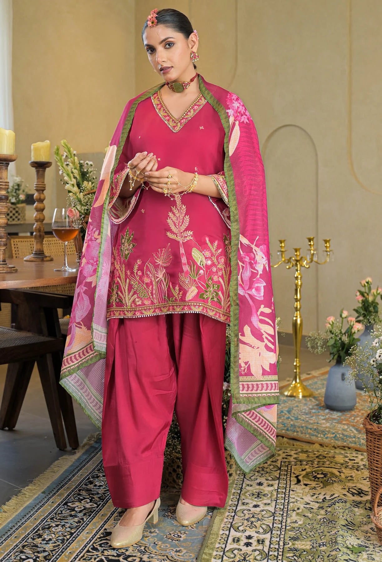 Woman in a pink traditional outfit with floral patterns in a decorated room.