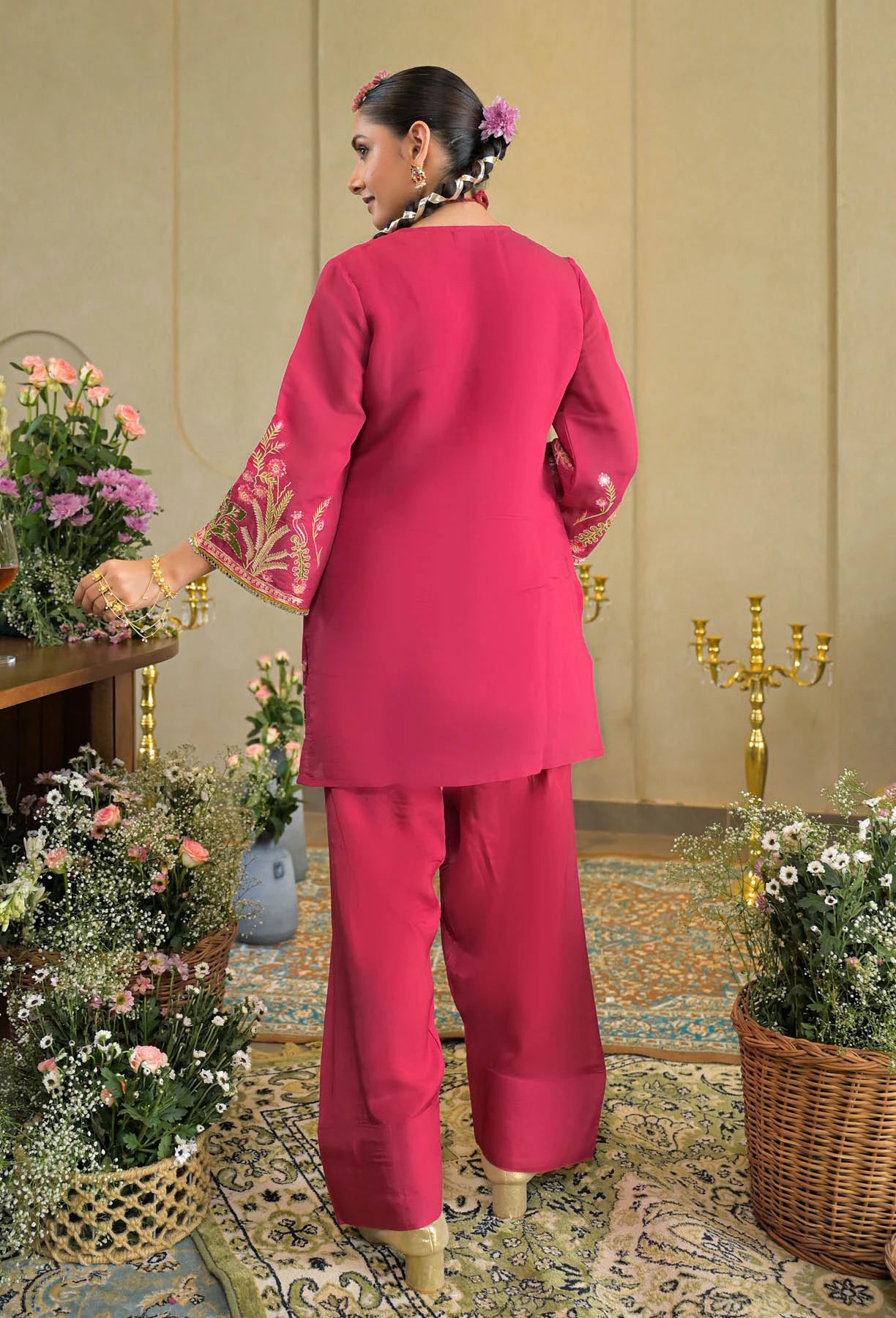 Woman in a pink traditional outfit standing in a decorated room with flowers and candles.