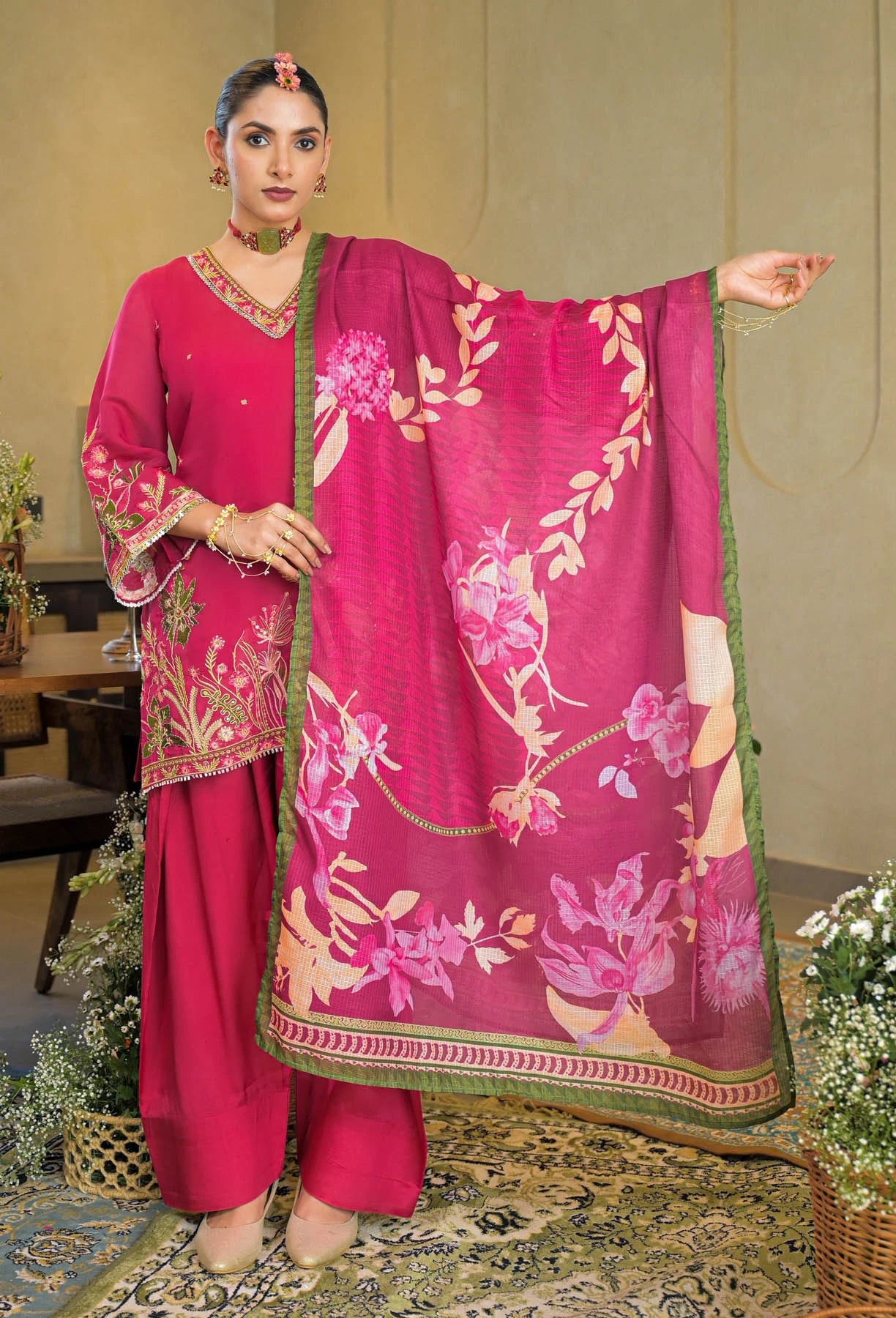 Woman in a pink traditional outfit with a floral dupatta in an indoor setting.