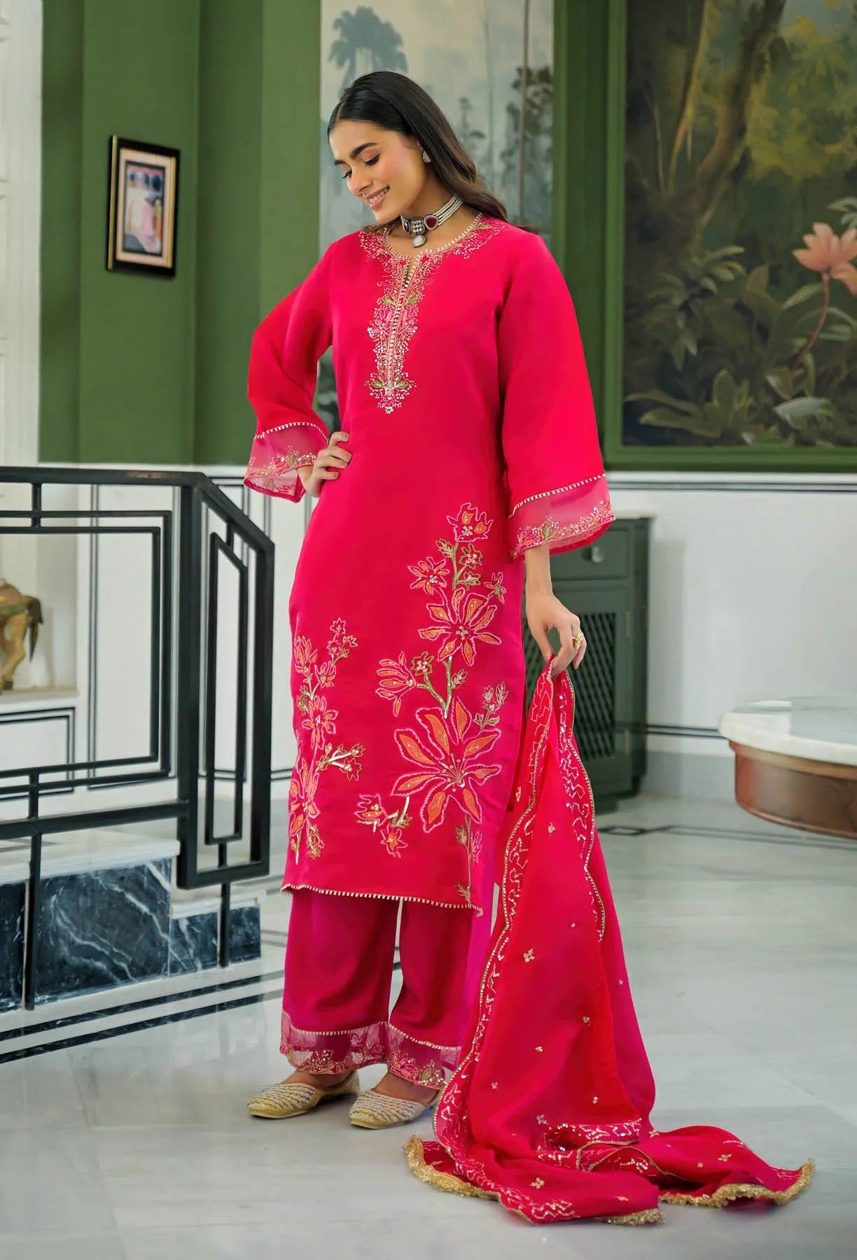 Woman in a bright pink traditional outfit with embroidery in an elegant interior setting.