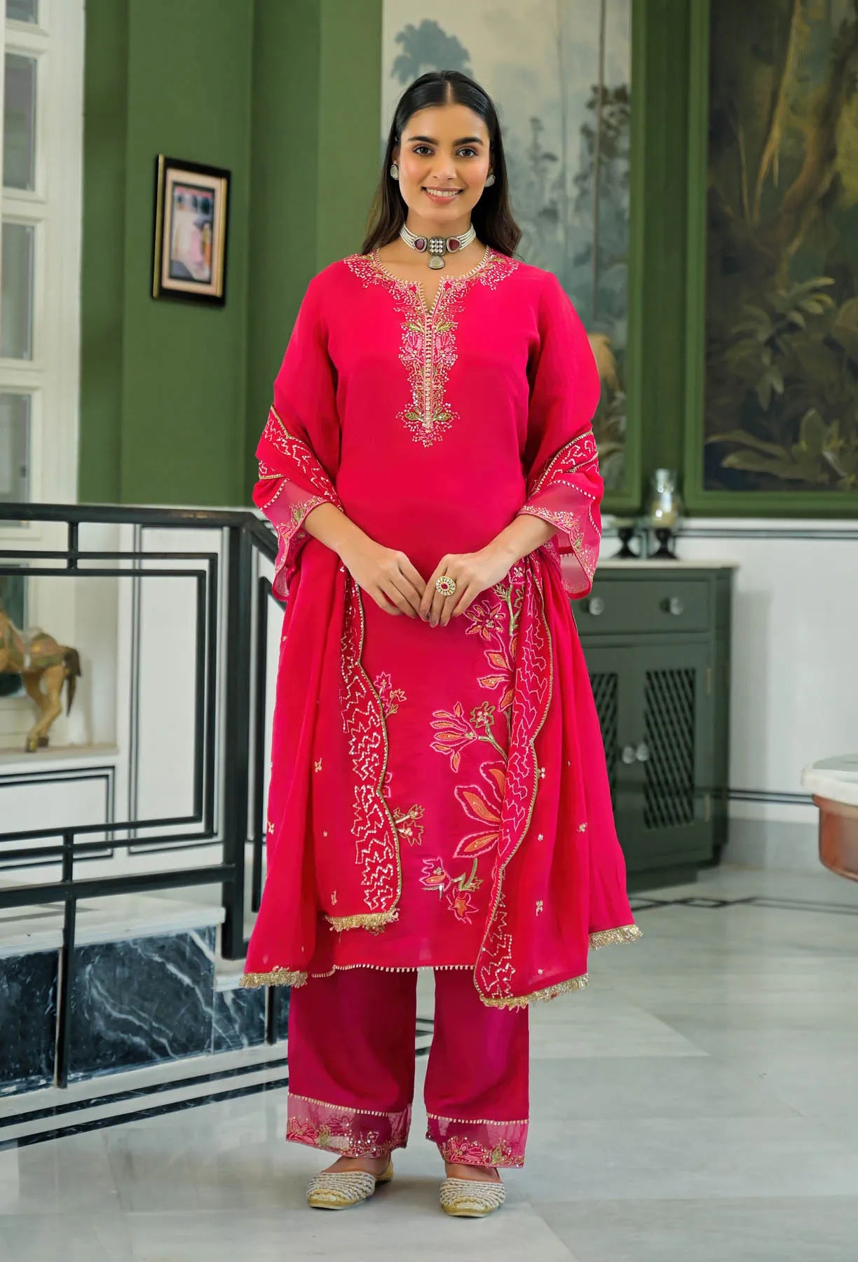 Woman in a pink traditional outfit standing in a room with green walls and decorative elements.