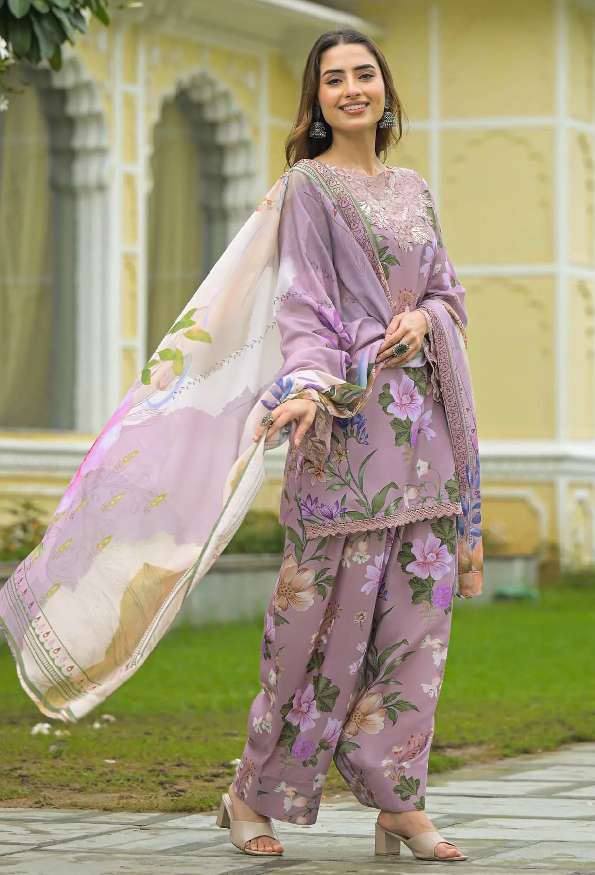 Woman in a floral outfit standing outdoors with a decorative building in the background