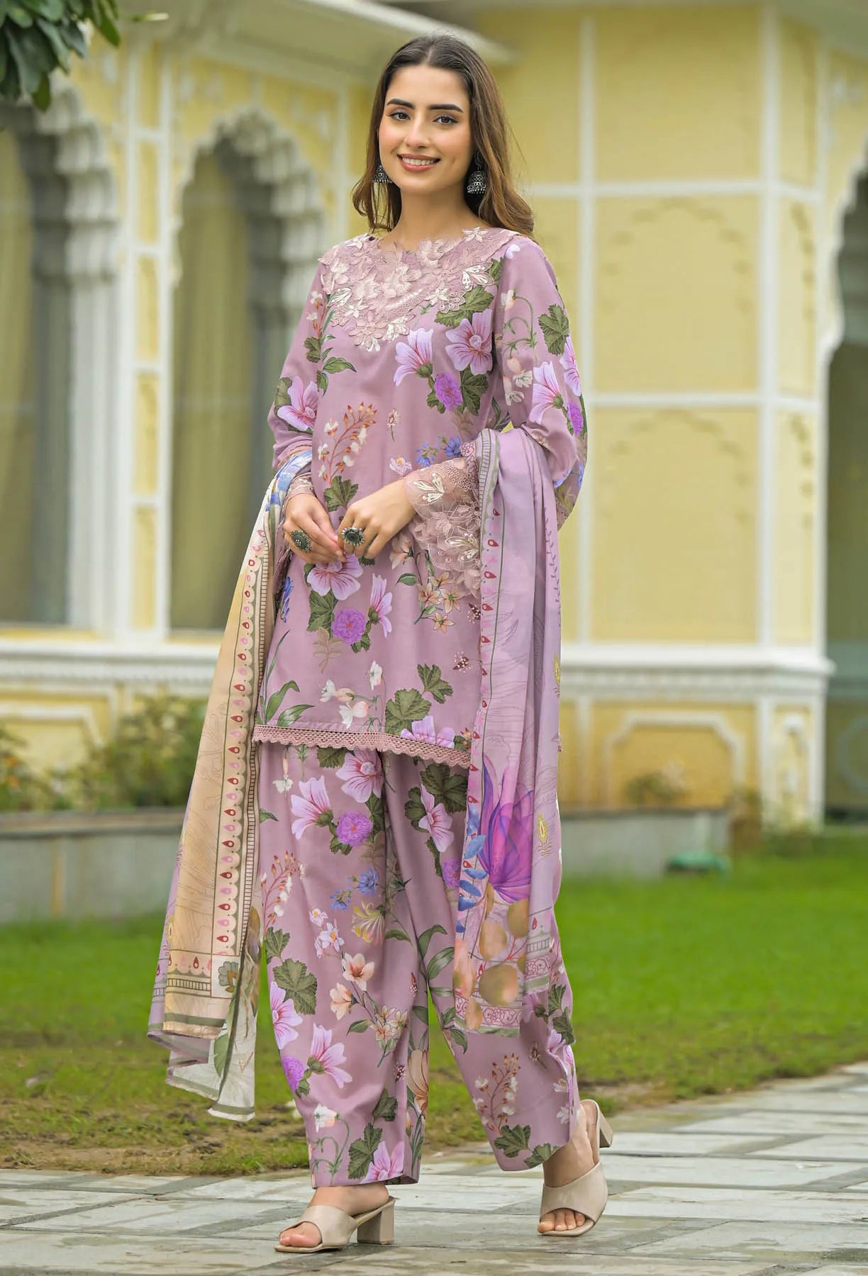 Woman in a pink floral outfit standing in front of a yellow building.
