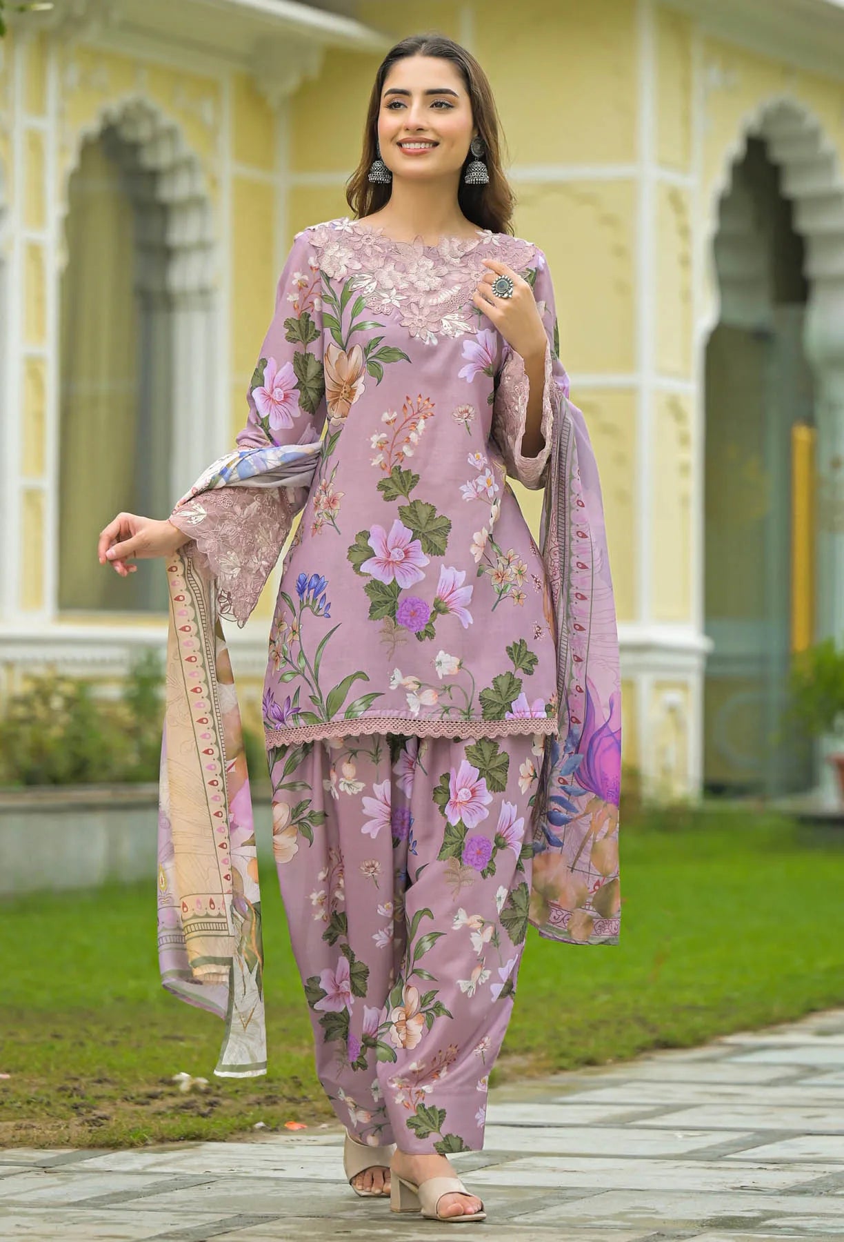 Woman in a floral outfit standing in front of a building with greenery.