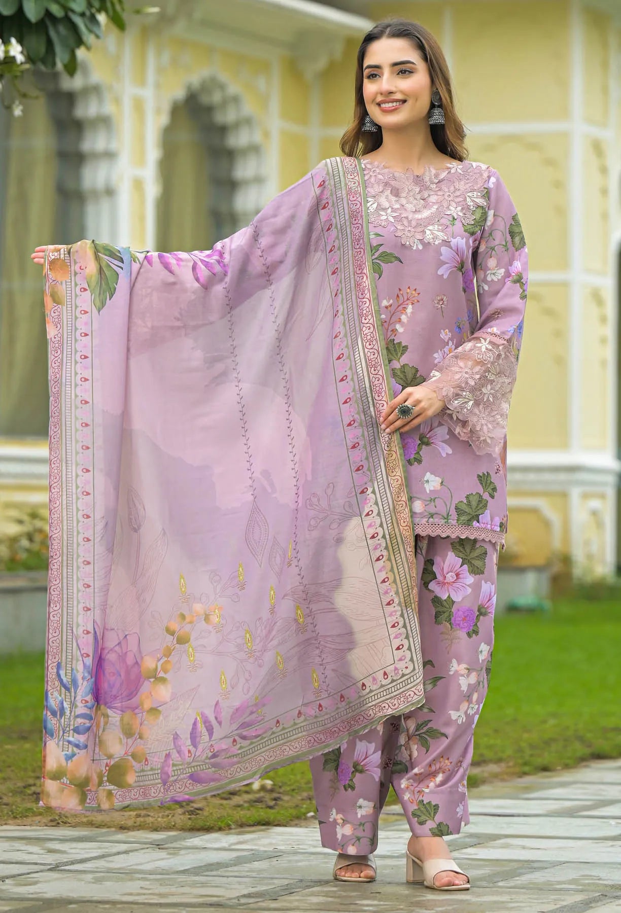 Woman wearing a purple floral outfit with a matching dupatta outdoors.