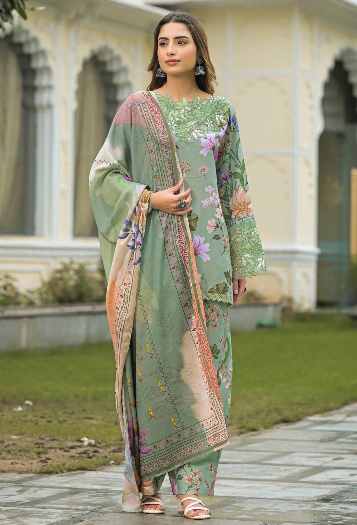 Woman in a green floral outfit standing outdoors with classical architecture in the background