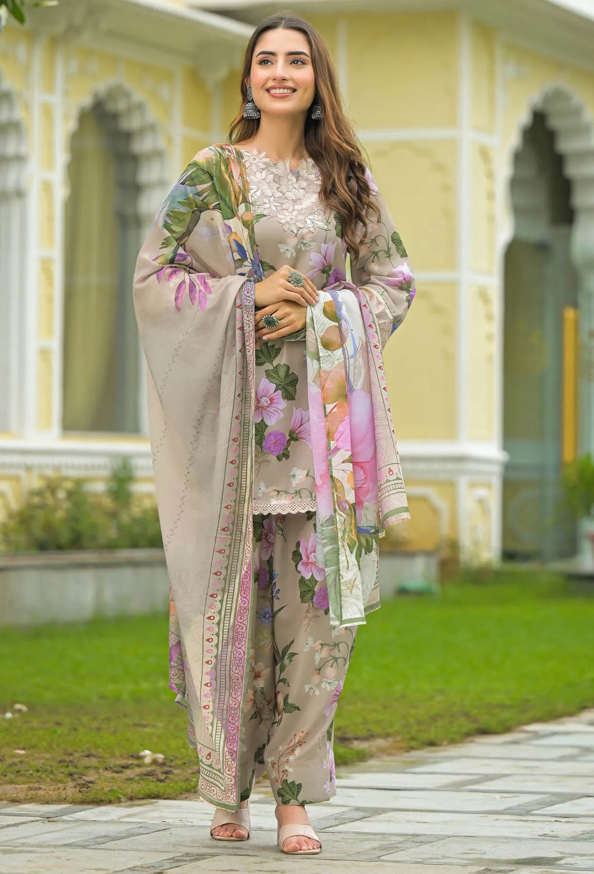 Woman in a floral outfit standing in front of a yellow building with greenery.